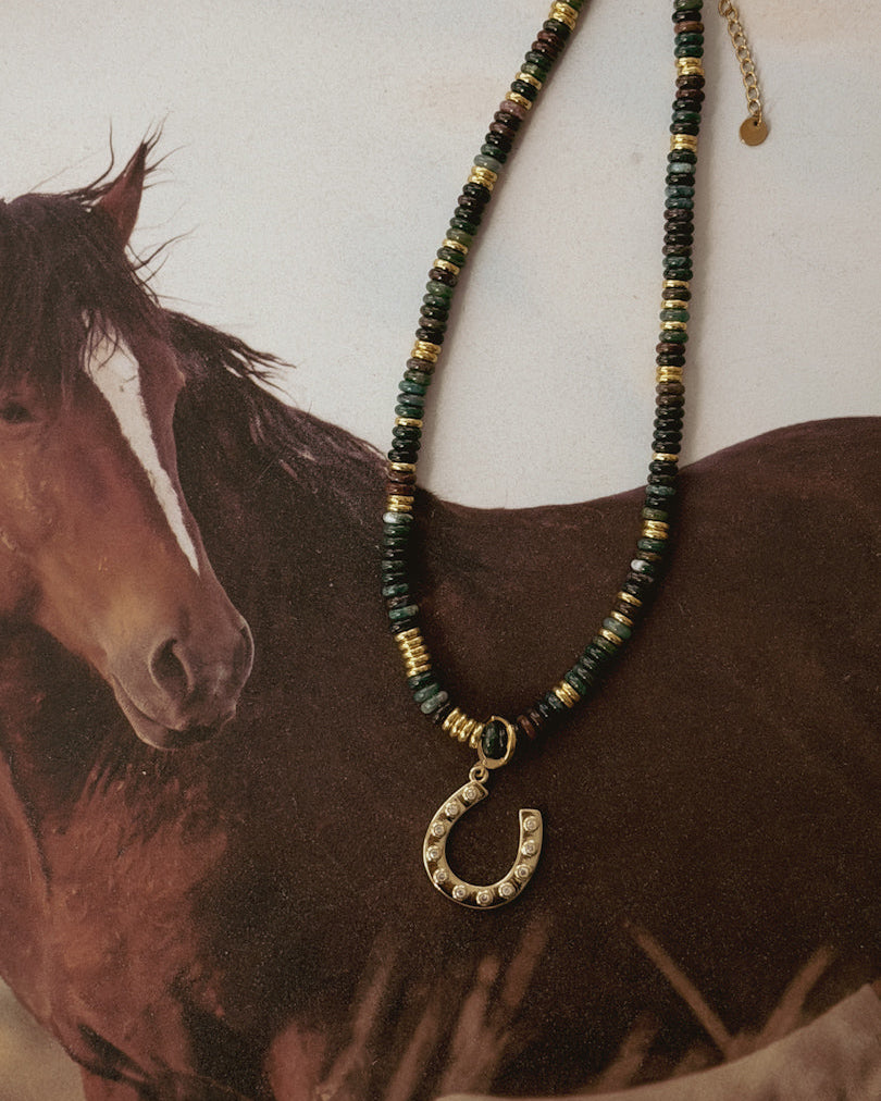 Western beaded necklace with gold horseshoe pendant displayed on horse background