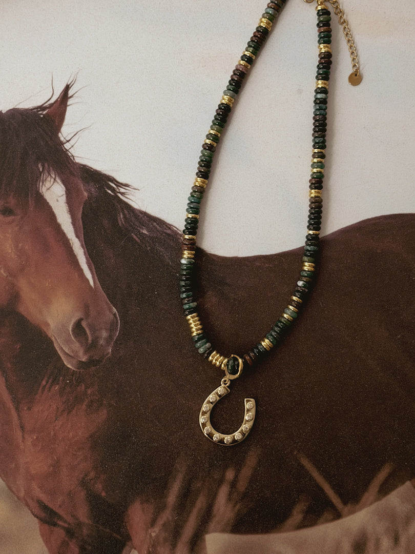 Western beaded necklace with gold horseshoe pendant displayed on horse background