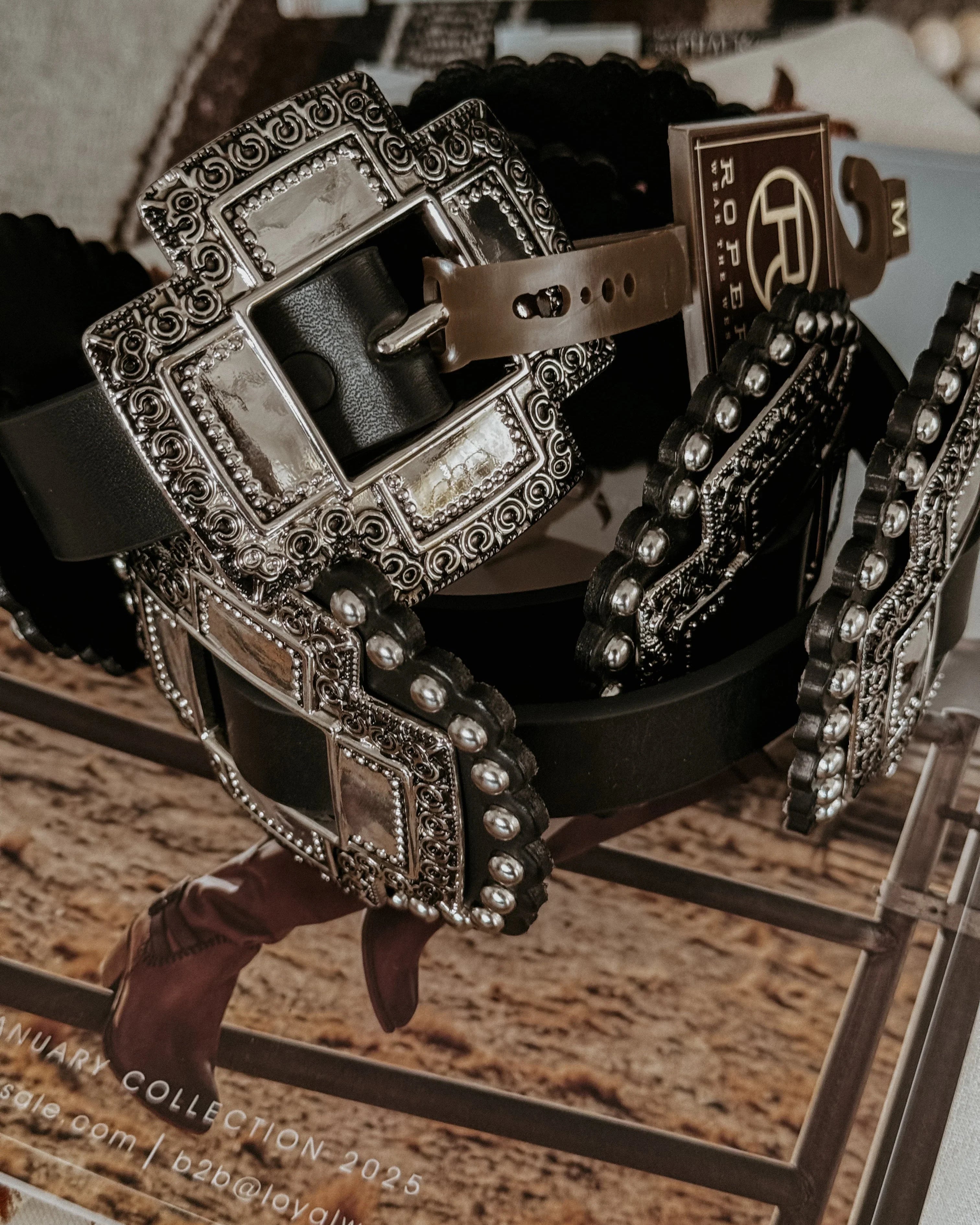 Black western belt with large ornate silver buckle and studs, styled on rustic background.