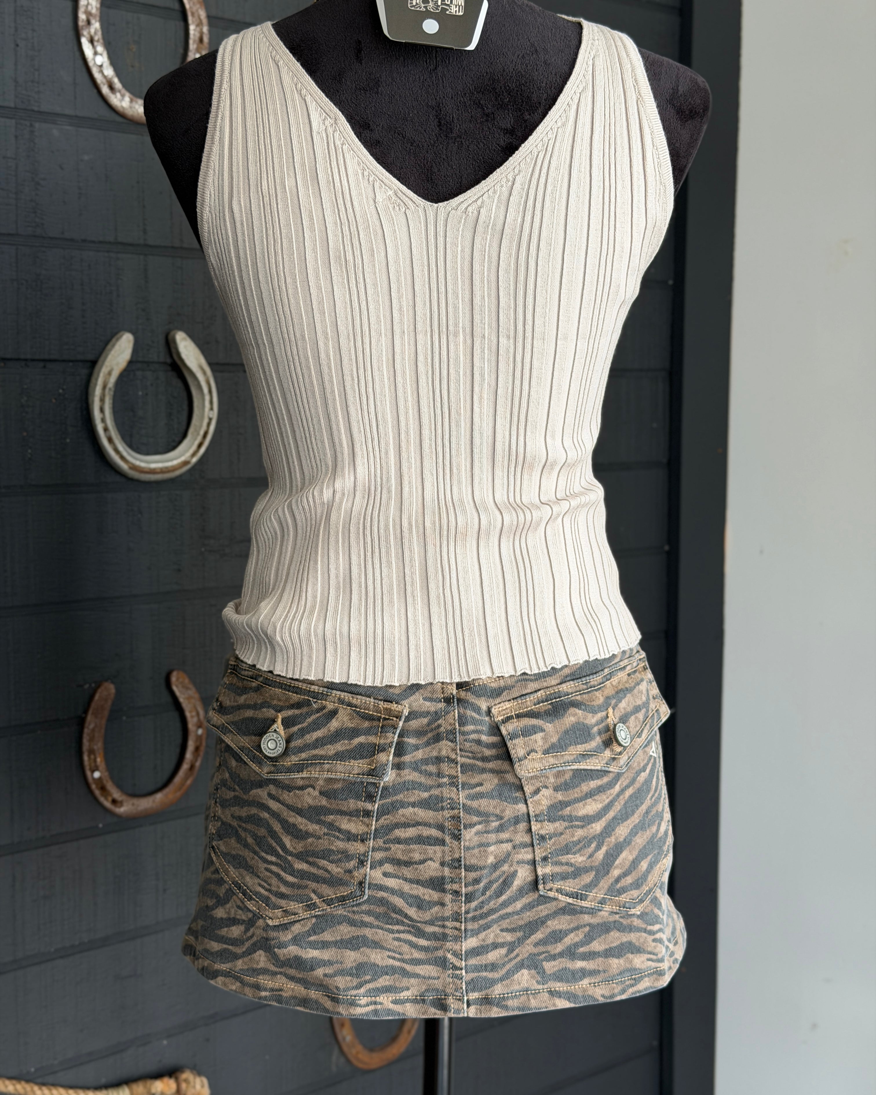 White ribbed tank top and zebra print shorts on a mannequin against a dark background with horseshoes.