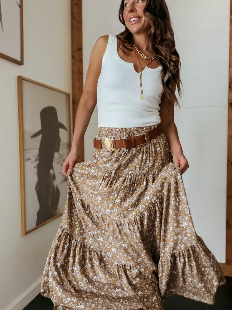 Woman wearing a white tank top and floral skirt with a brown belt, standing indoors.