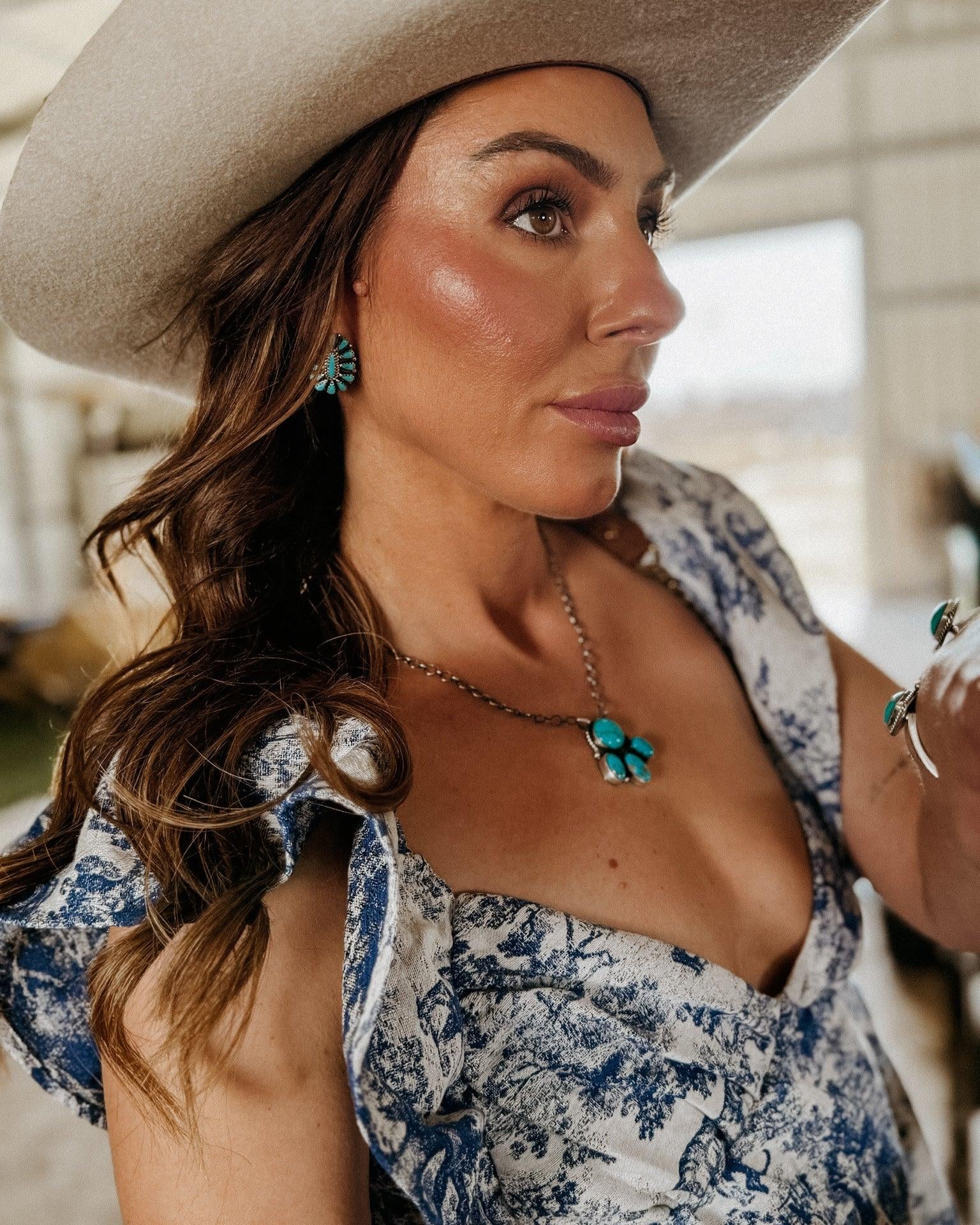 Woman in a cream cowboy hat wearing turquoise western jewelry and blue floral dress