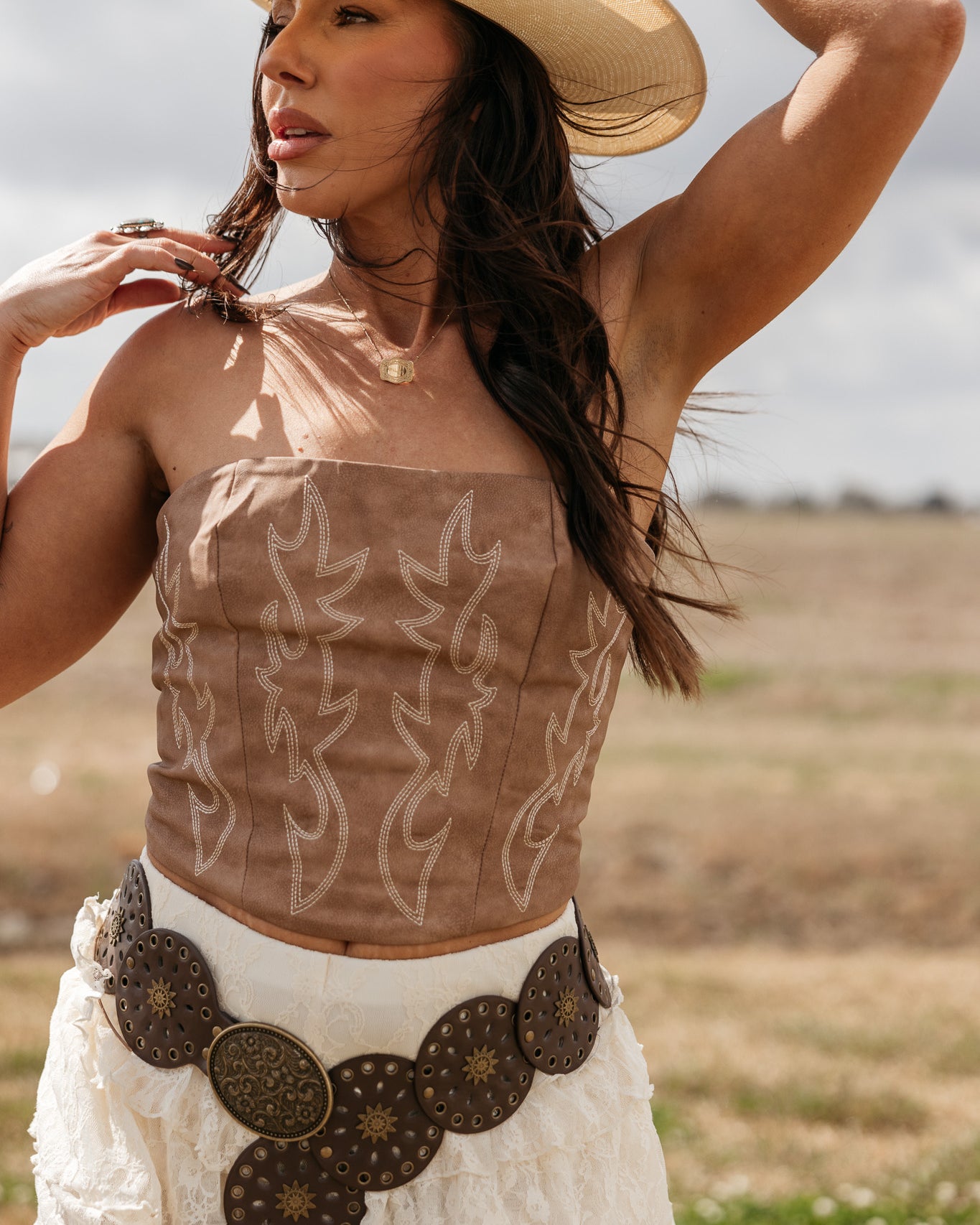 Woman in cowgirl hat, embroidered suede corset top, lace skirt, and western concho belt outdoors