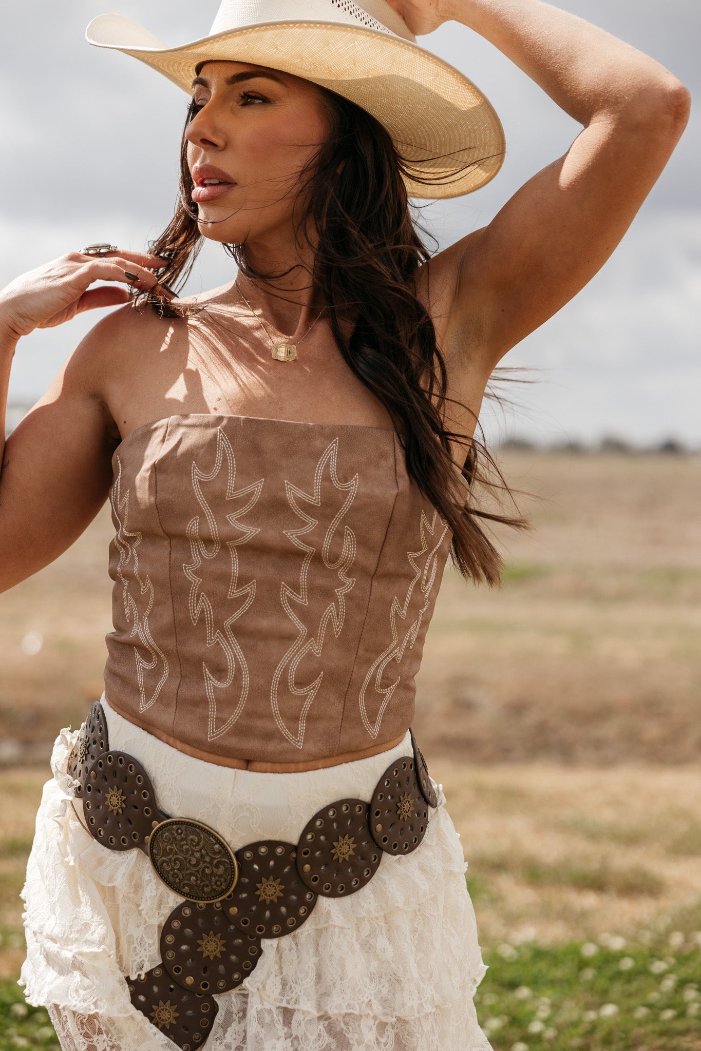 Woman in cowgirl hat, embroidered suede corset top, lace skirt, and western concho belt outdoors