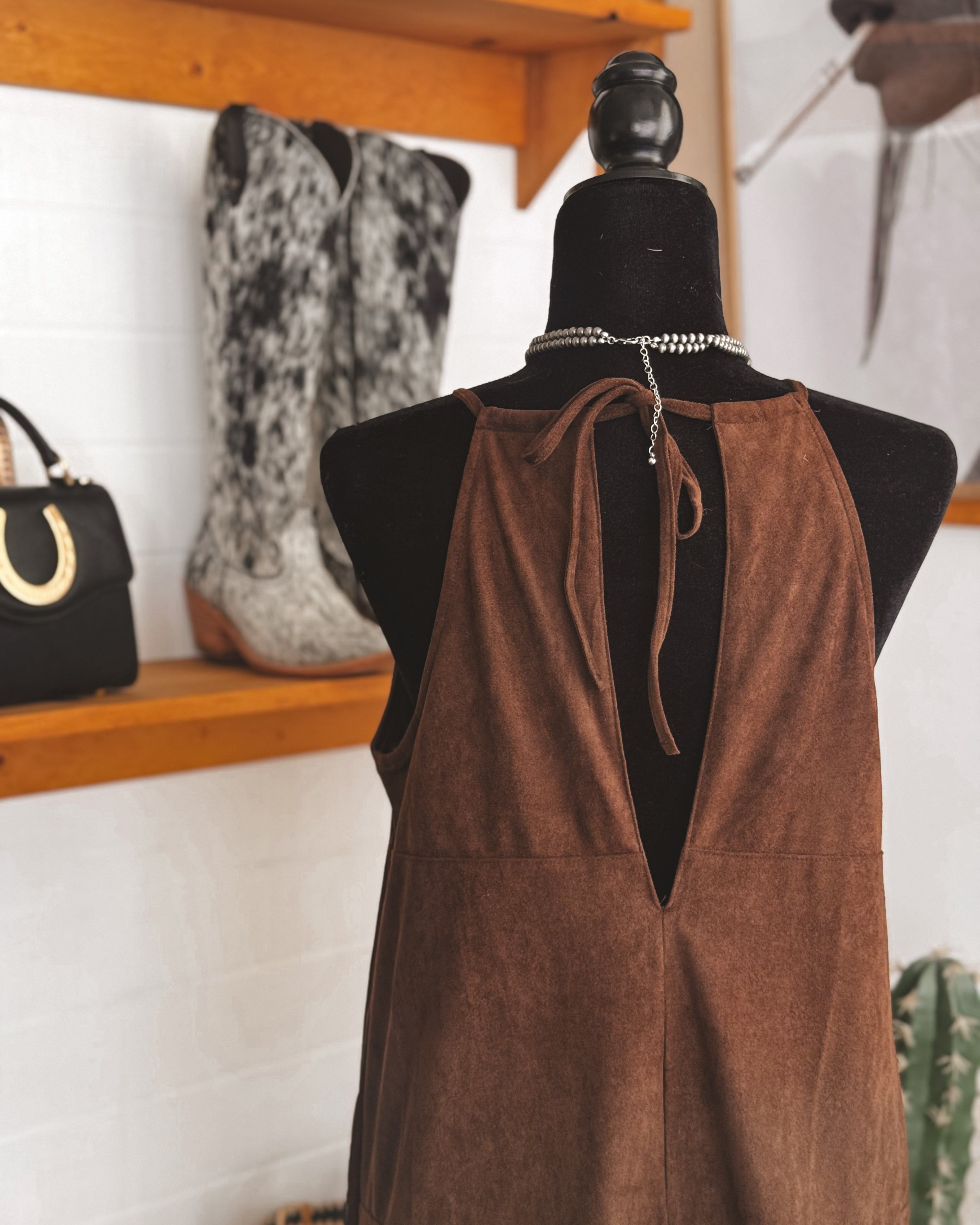 Brown suede western dress on mannequin, cowgirl boots and western bag in boutique setting