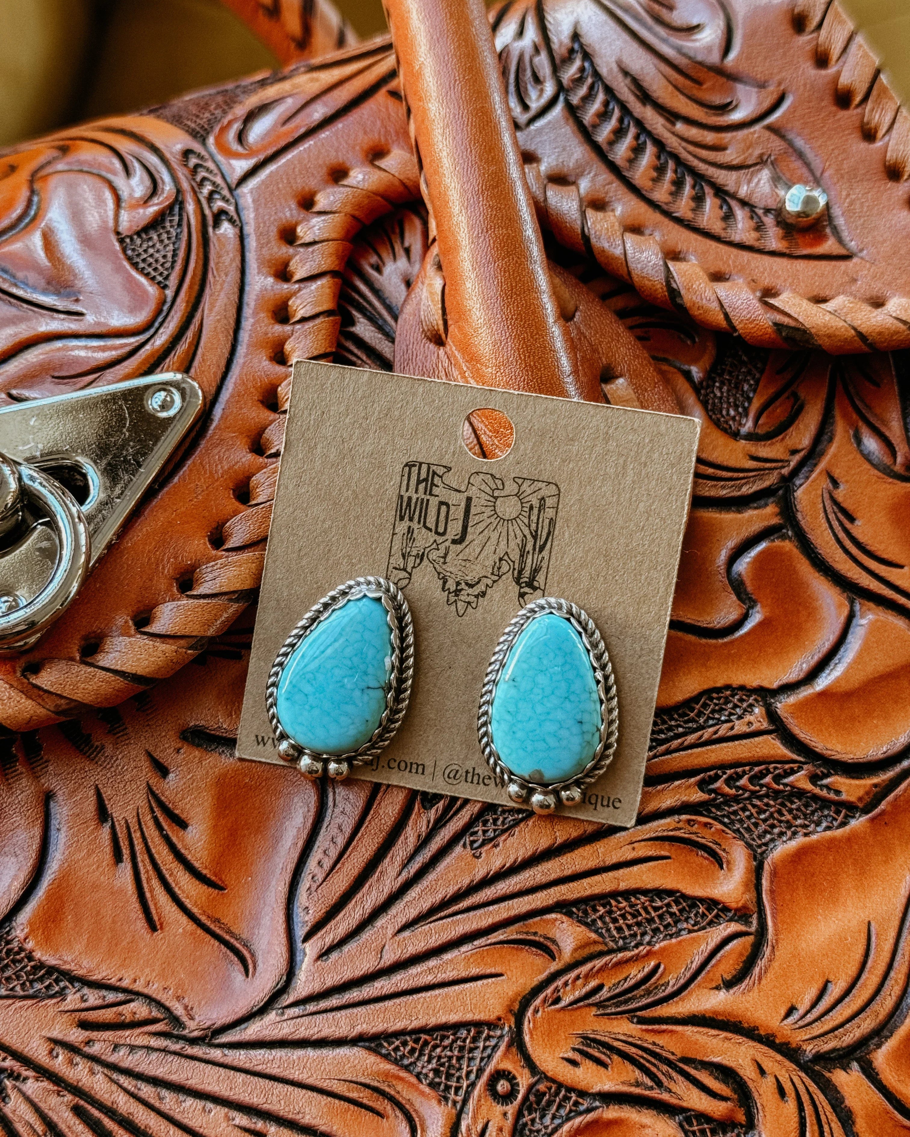 Turquoise western earrings with silver rope detail on tooled leather purse background