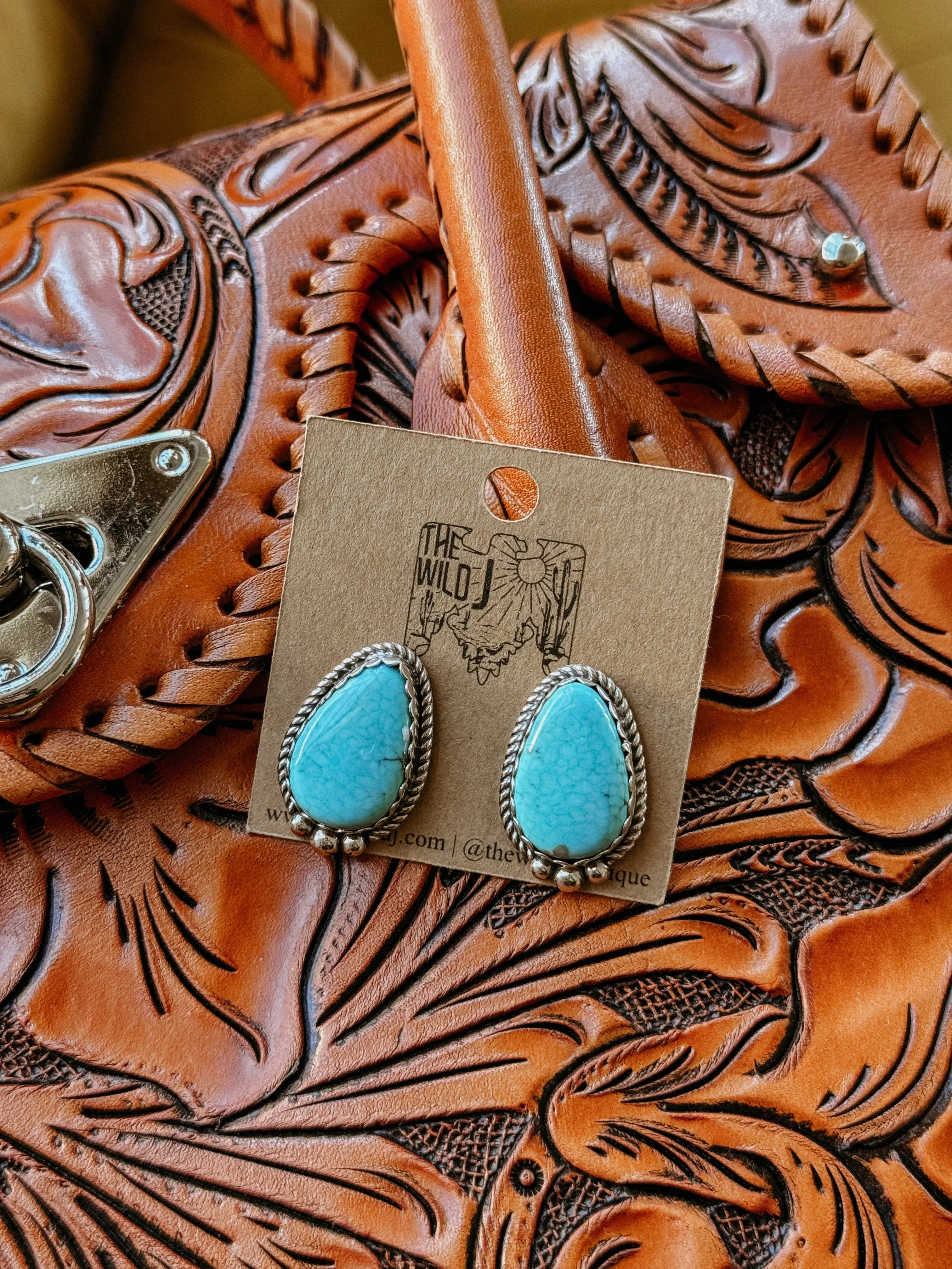 Turquoise western earrings with silver rope detail on tooled leather purse background