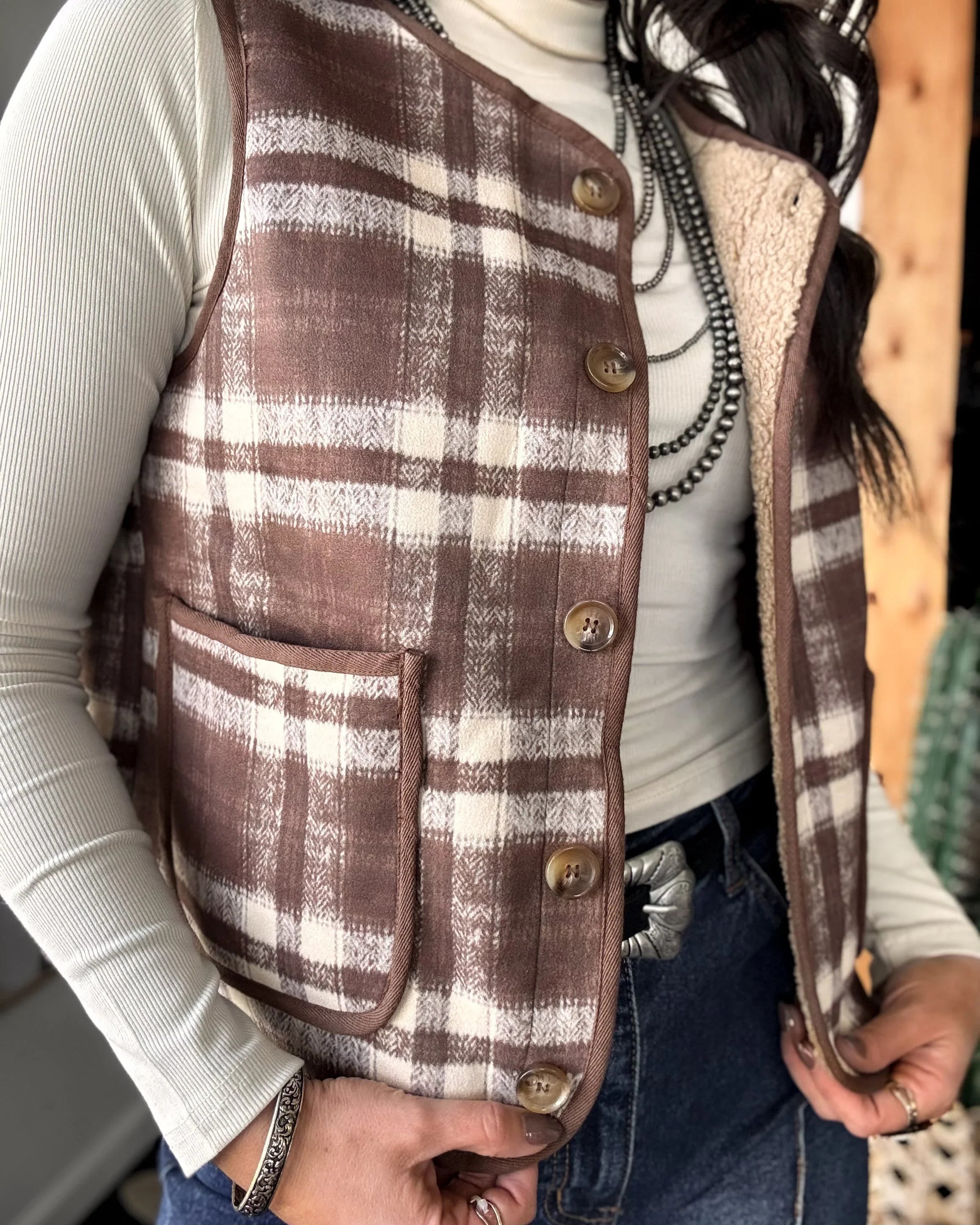 Person wearing a brown plaid vest over a white shirt with a blurred background