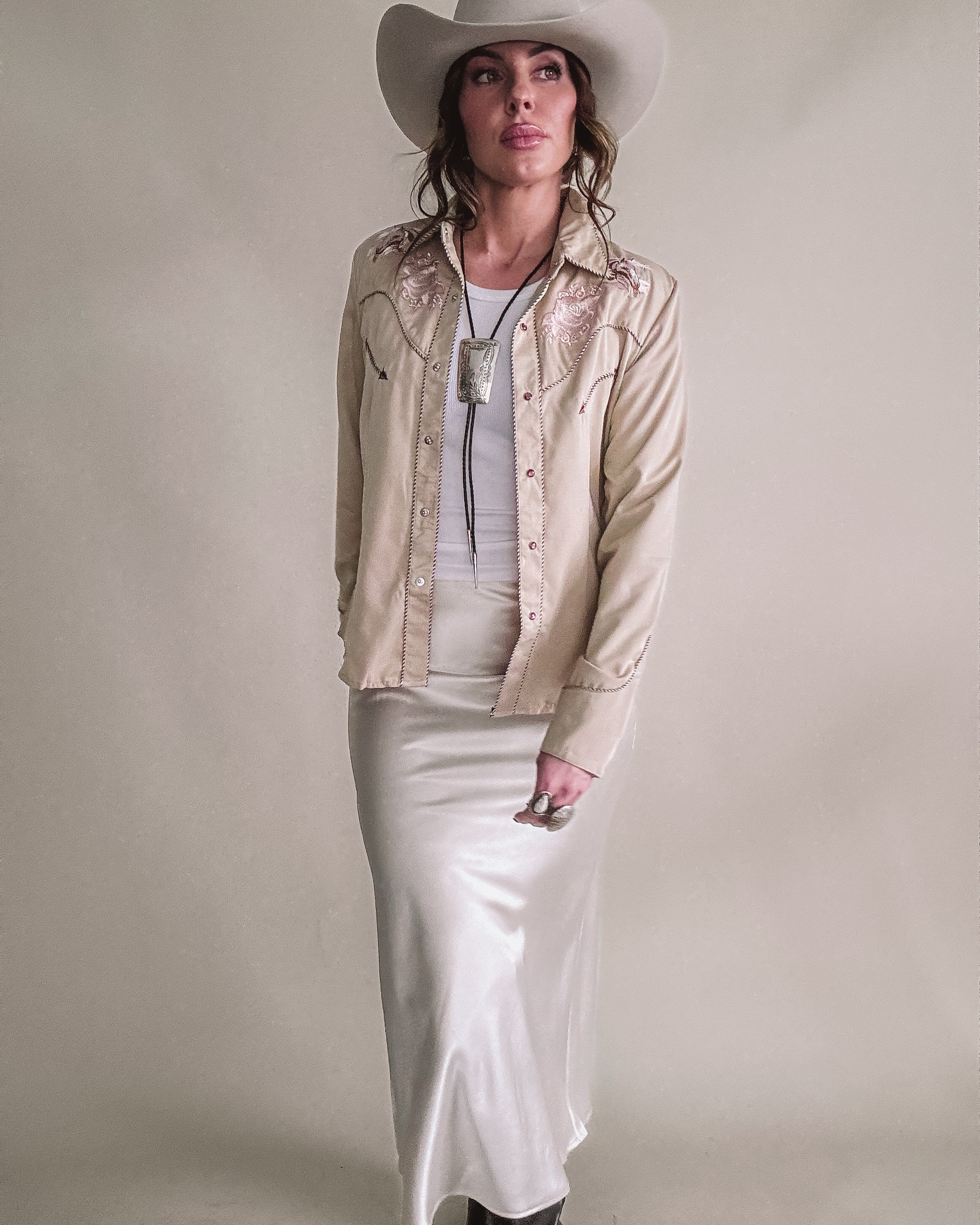 Woman in western boho outfit with cream cowgirl hat, embroidered shirt, satin skirt, and boots