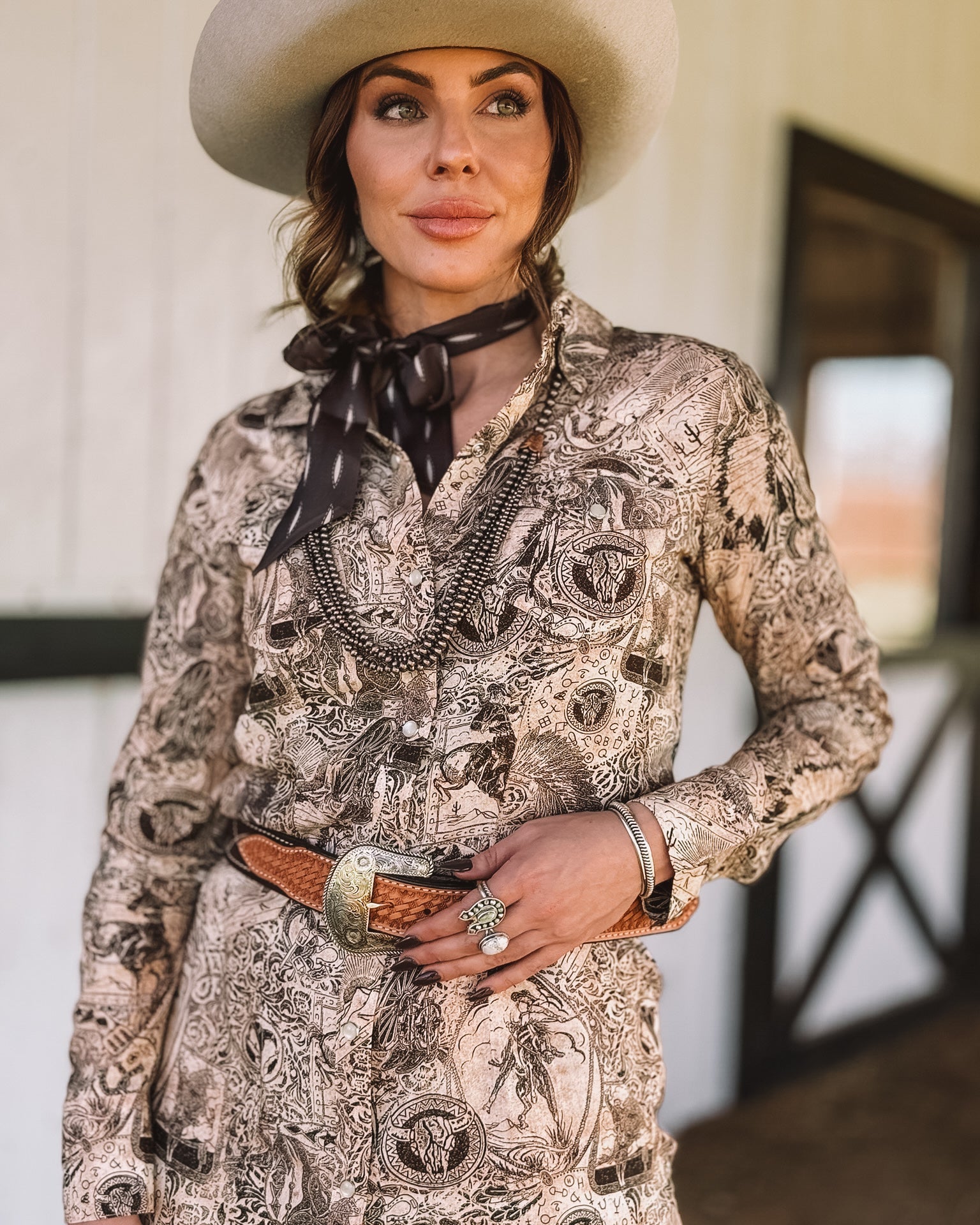 Woman in western cowboy hat, printed boho shirt, concho belt, and western jewelry outdoors