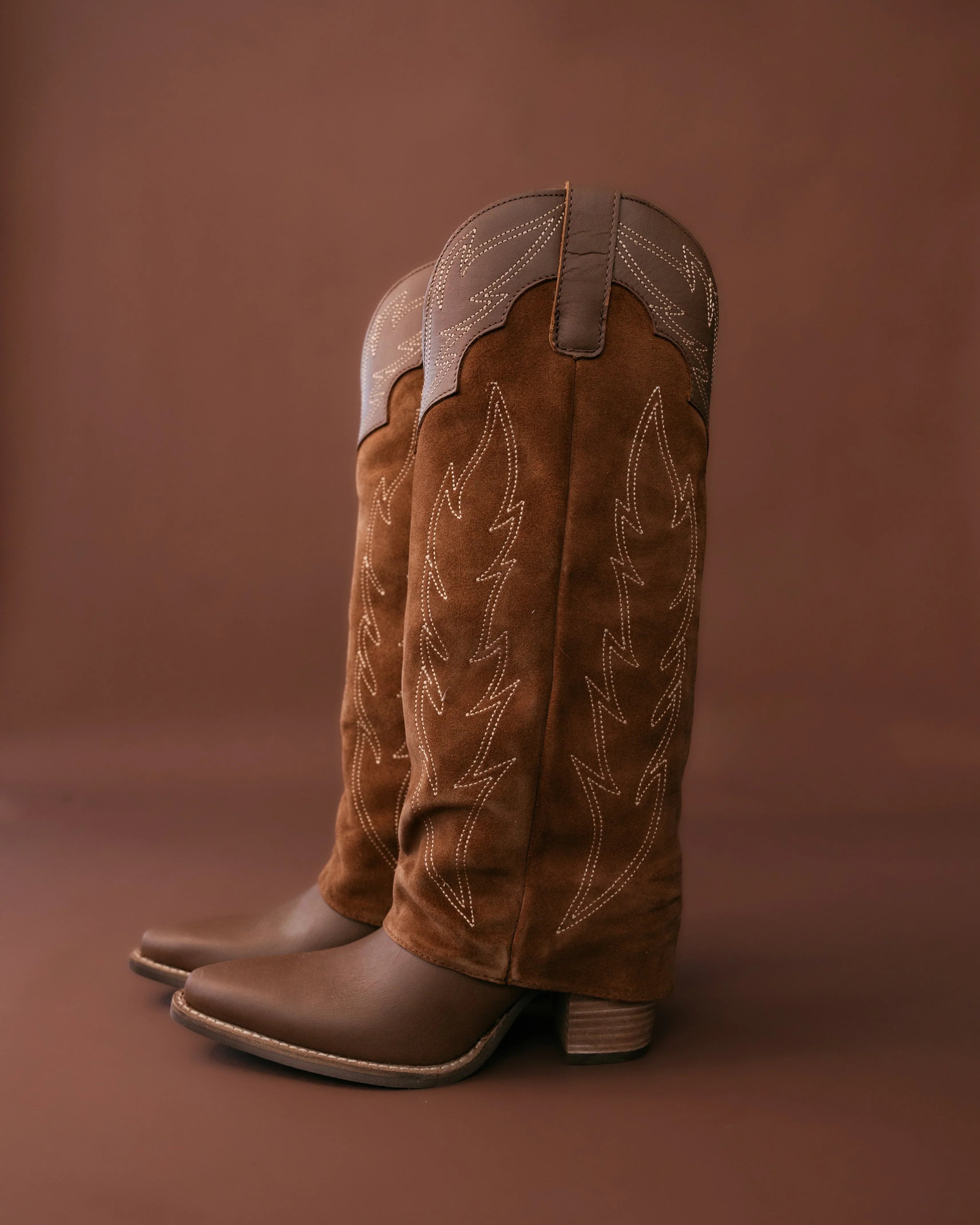 Pair of brown cowboy boots with white stitching on a brown background