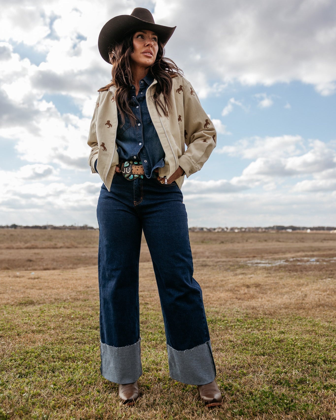Woman in cowgirl hat, western jacket, denim shirt, wide-leg jeans and boots outdoors