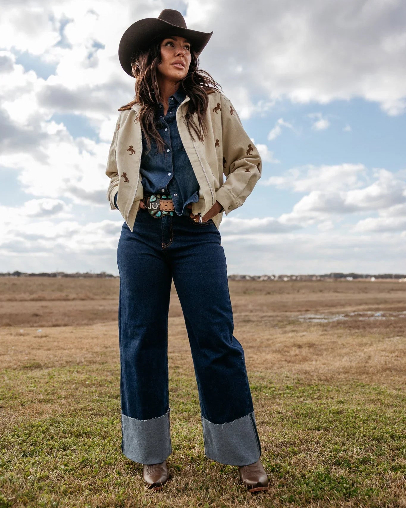 Woman in cowgirl hat, western jacket, denim shirt, wide-leg jeans and boots outdoors