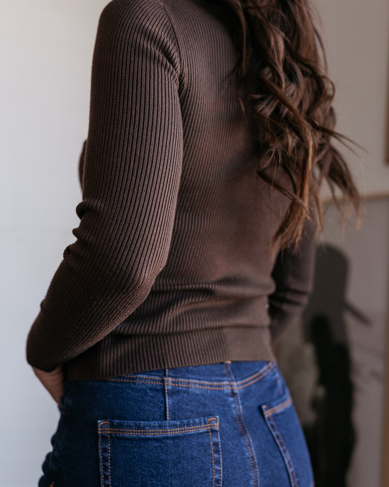 Woman wearing a brown ribbed sweater and high-waisted blue jeans, western casual style