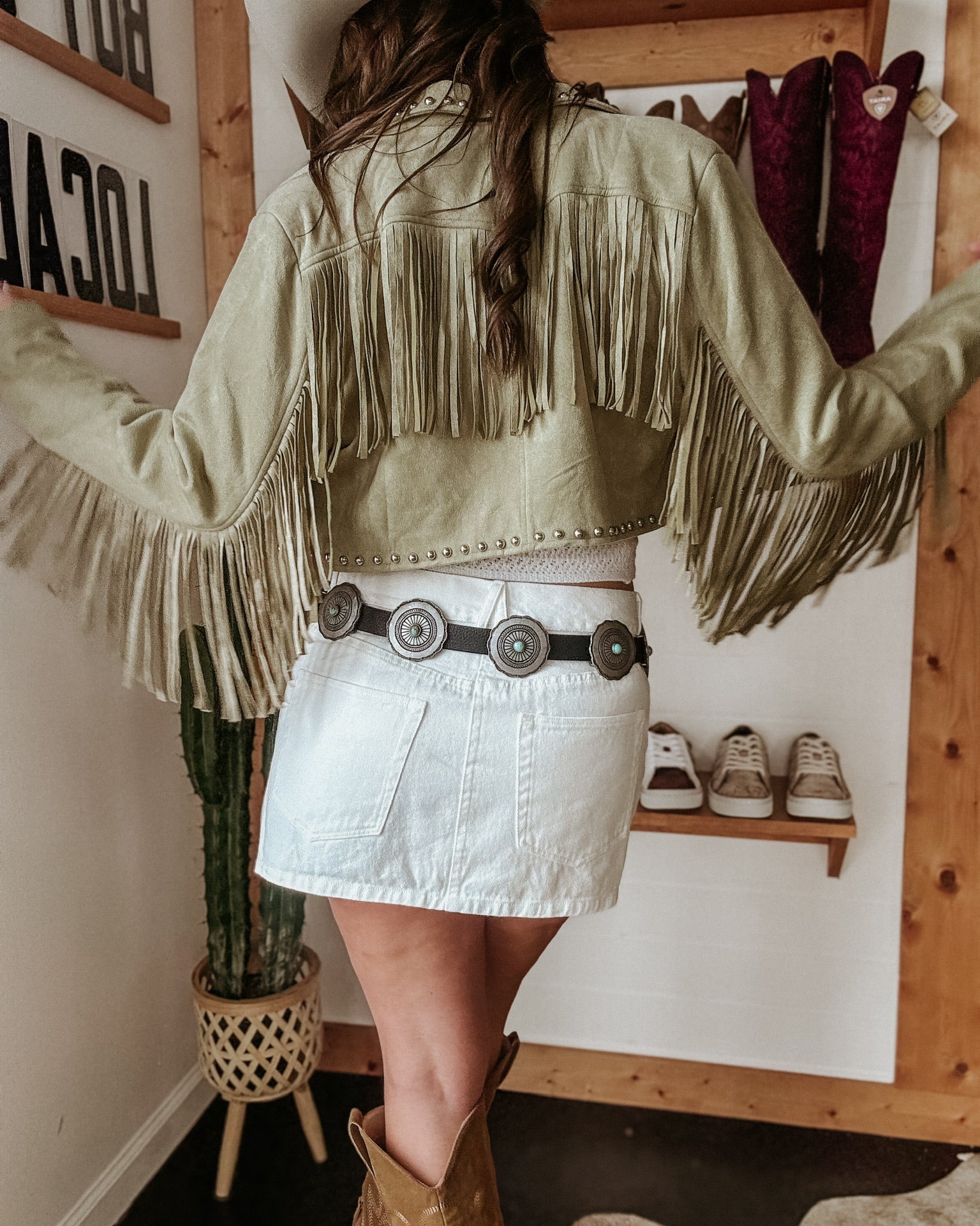 Woman in fringed suede jacket, white denim skirt, western belt and cowboy boots, boho style outfit