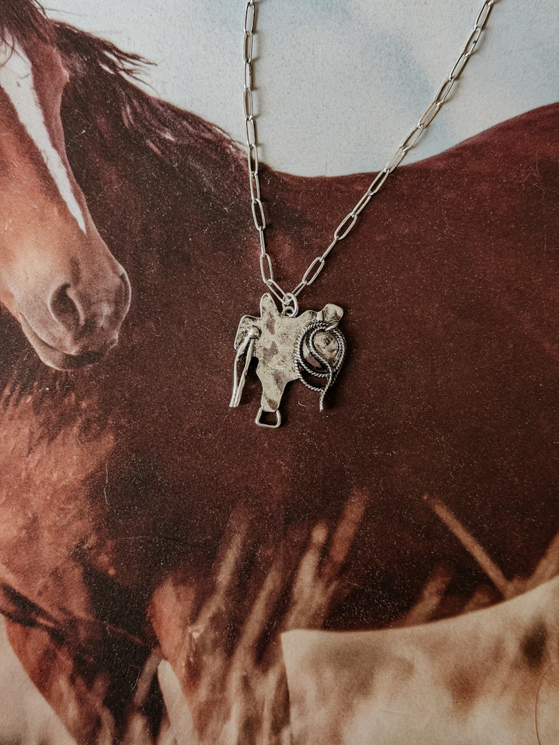 Western cowgirl necklace with horse and saddle pendant on horse background