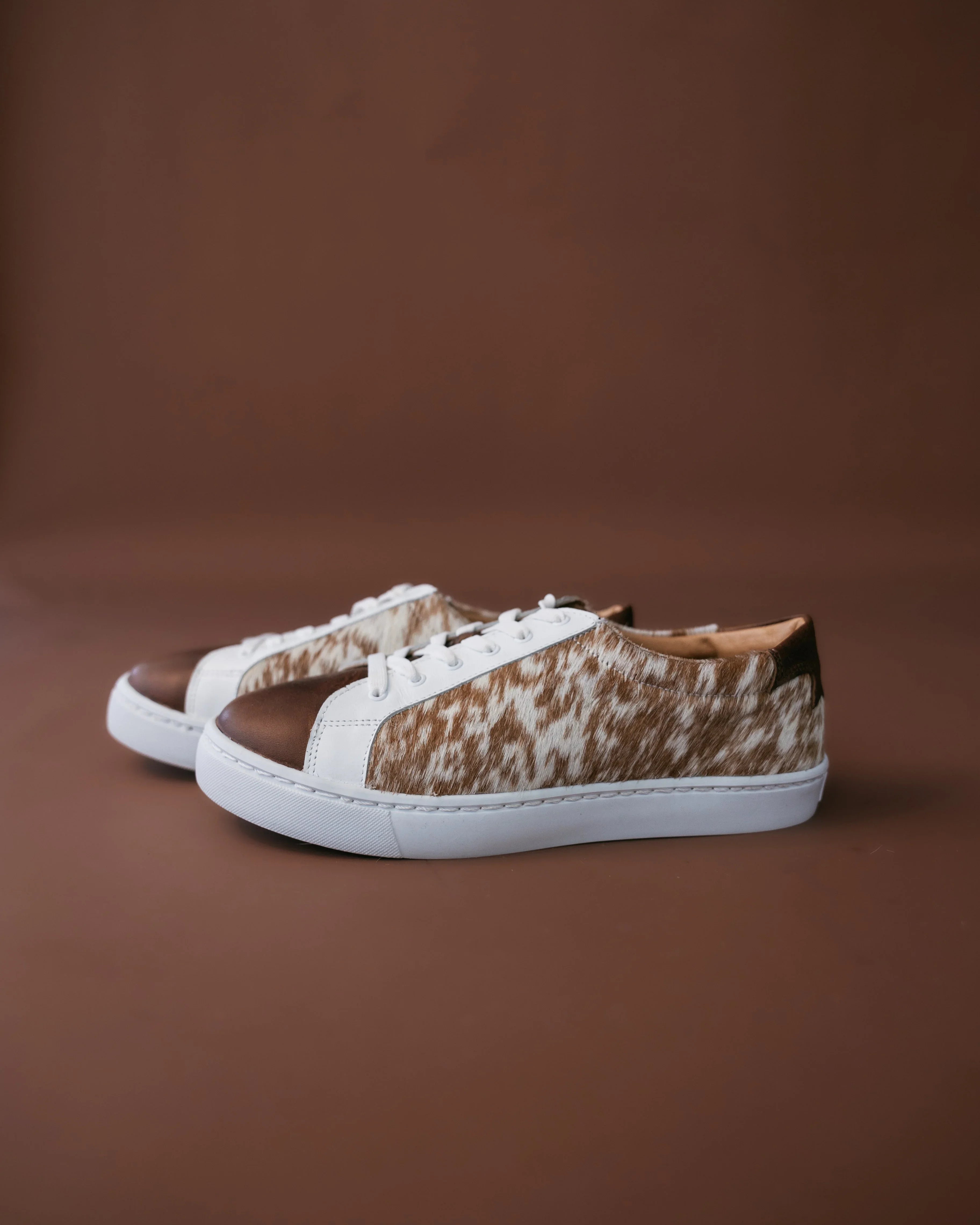 Brown and white cow print western sneakers with white soles on a brown background