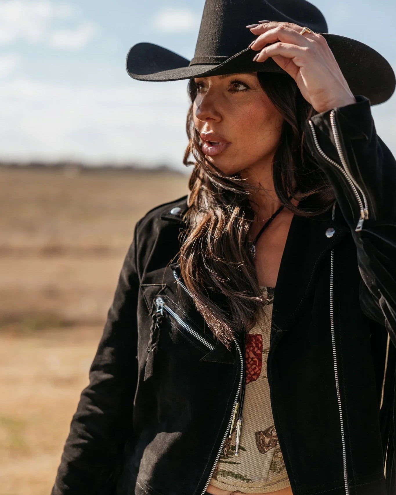 Woman in black cowboy hat and suede western jacket in outdoor boho setting