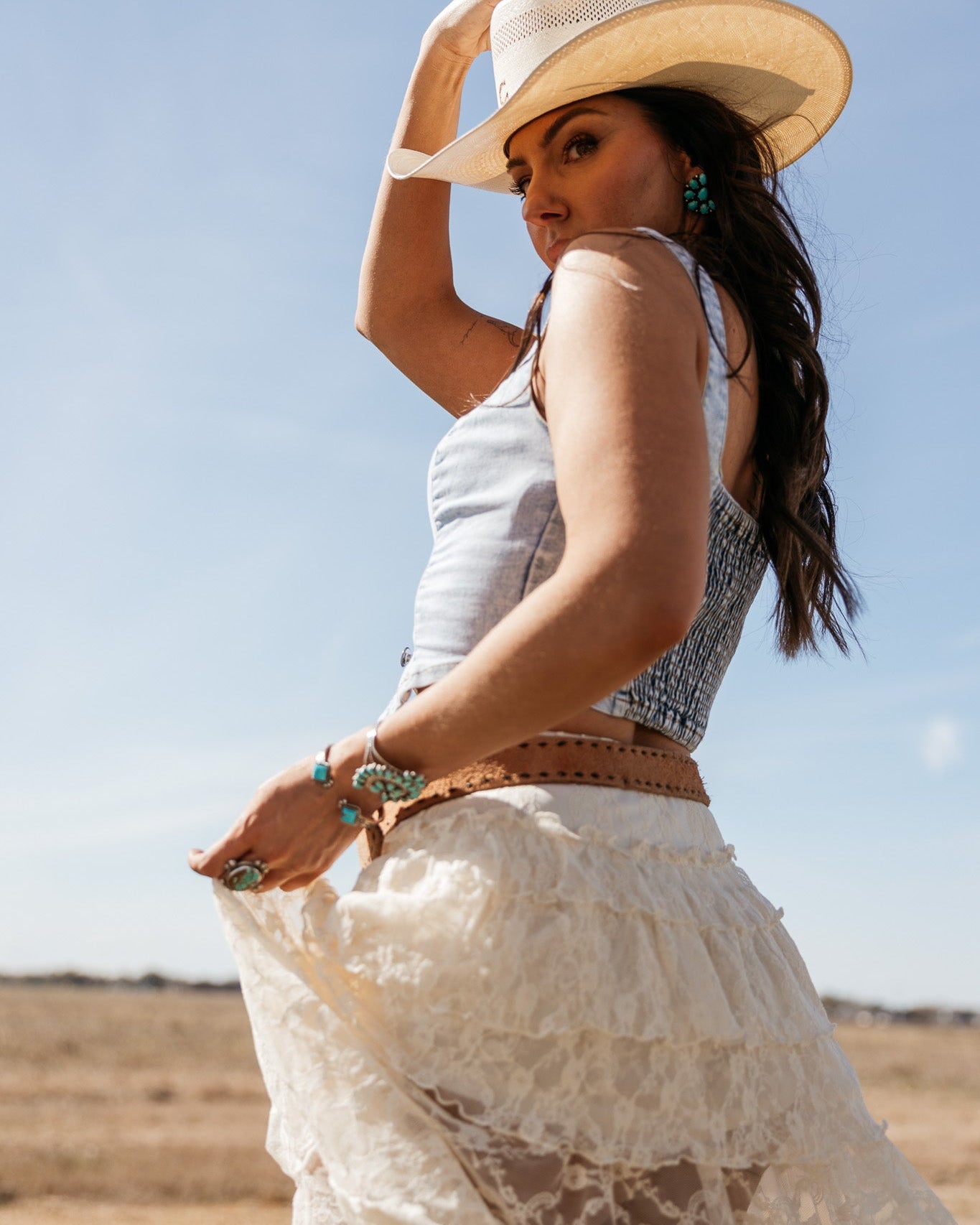 Woman in a white lace skirt, denim top, and cowboy hat in a western boho outdoor setting