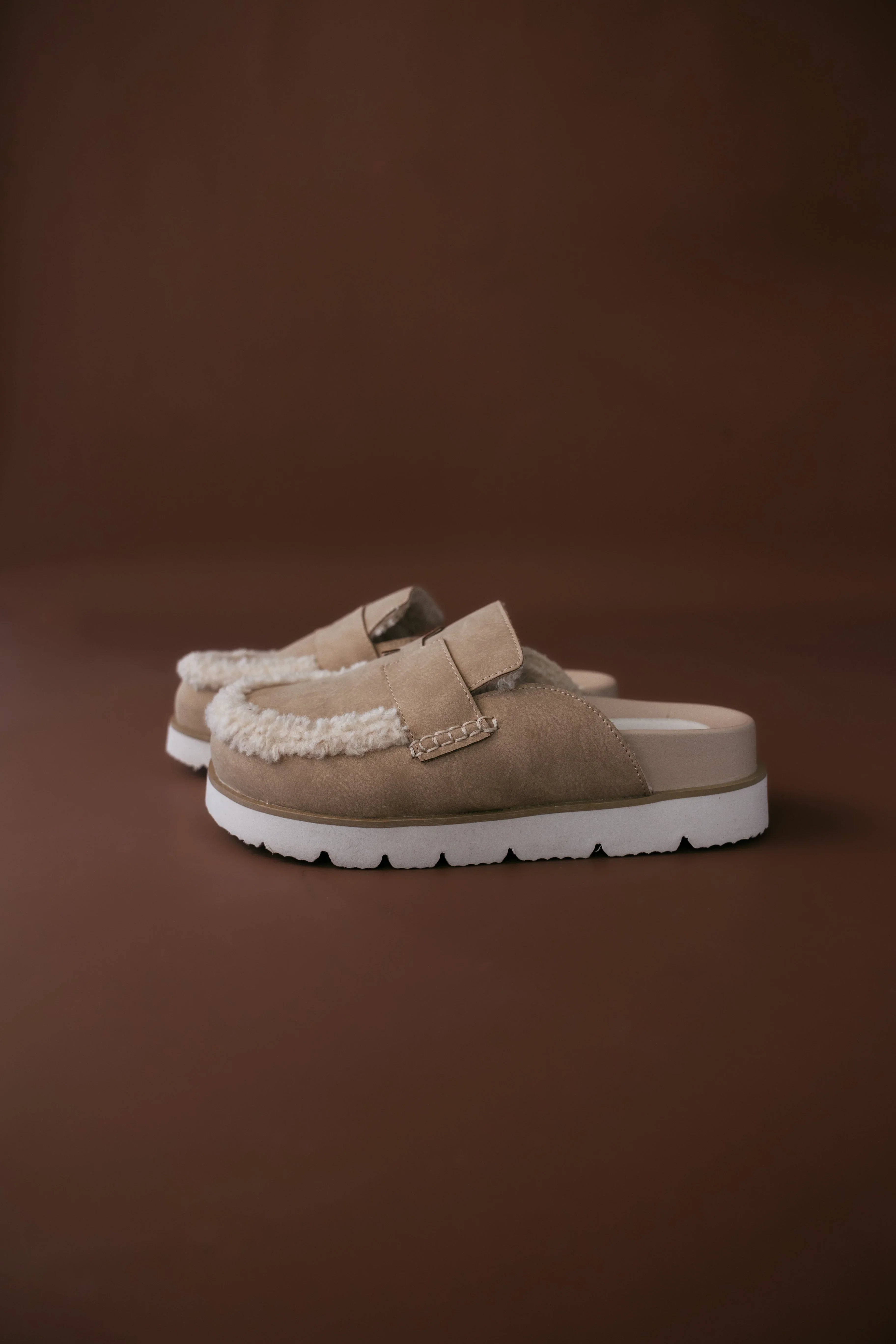 Pair of tan slippers with white soles on a brown background