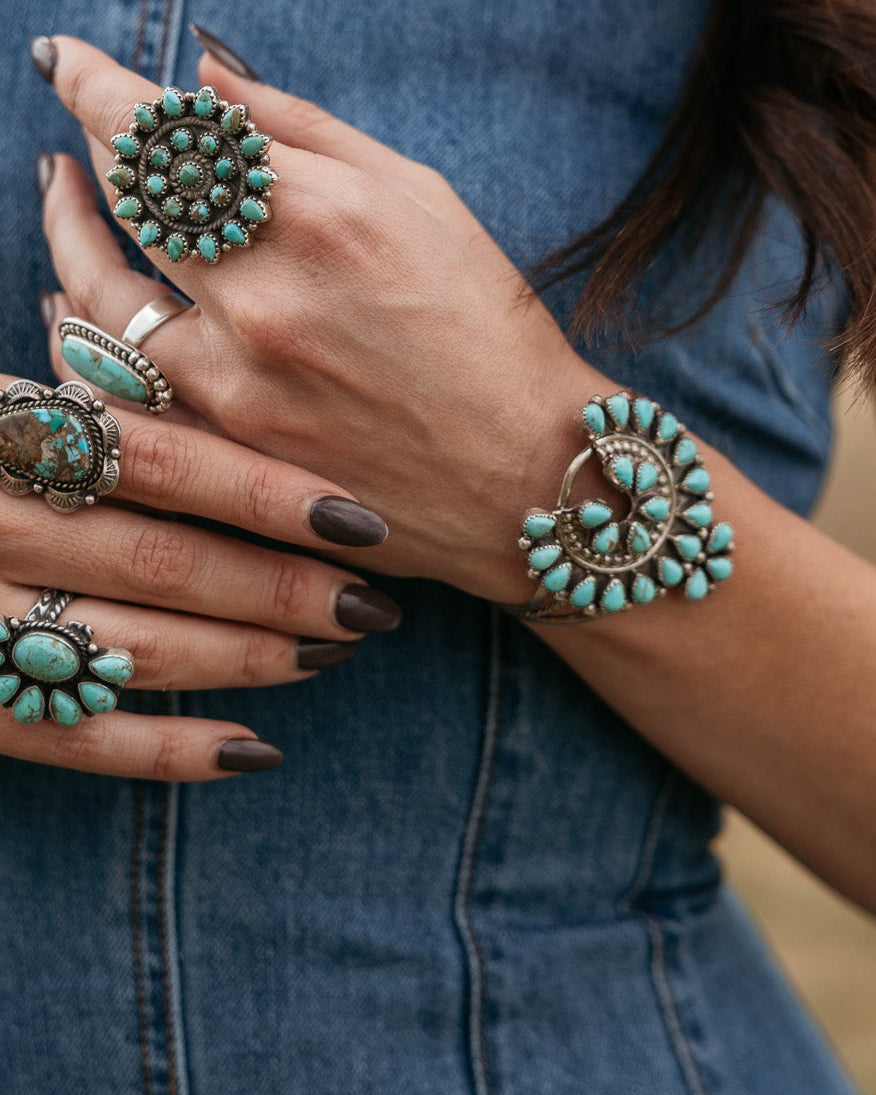 Woman wearing multiple turquoise western rings and bracelet with denim dress