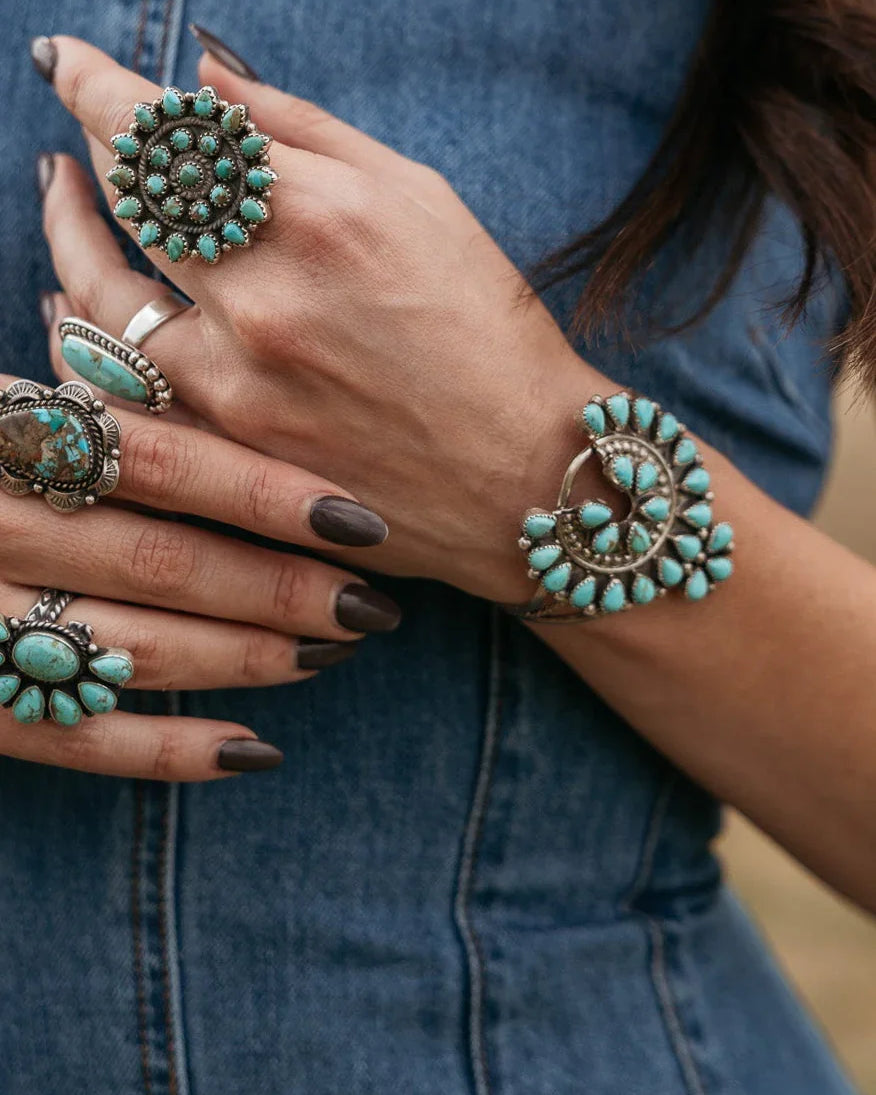 Woman wearing multiple turquoise western rings and bracelet with denim dress