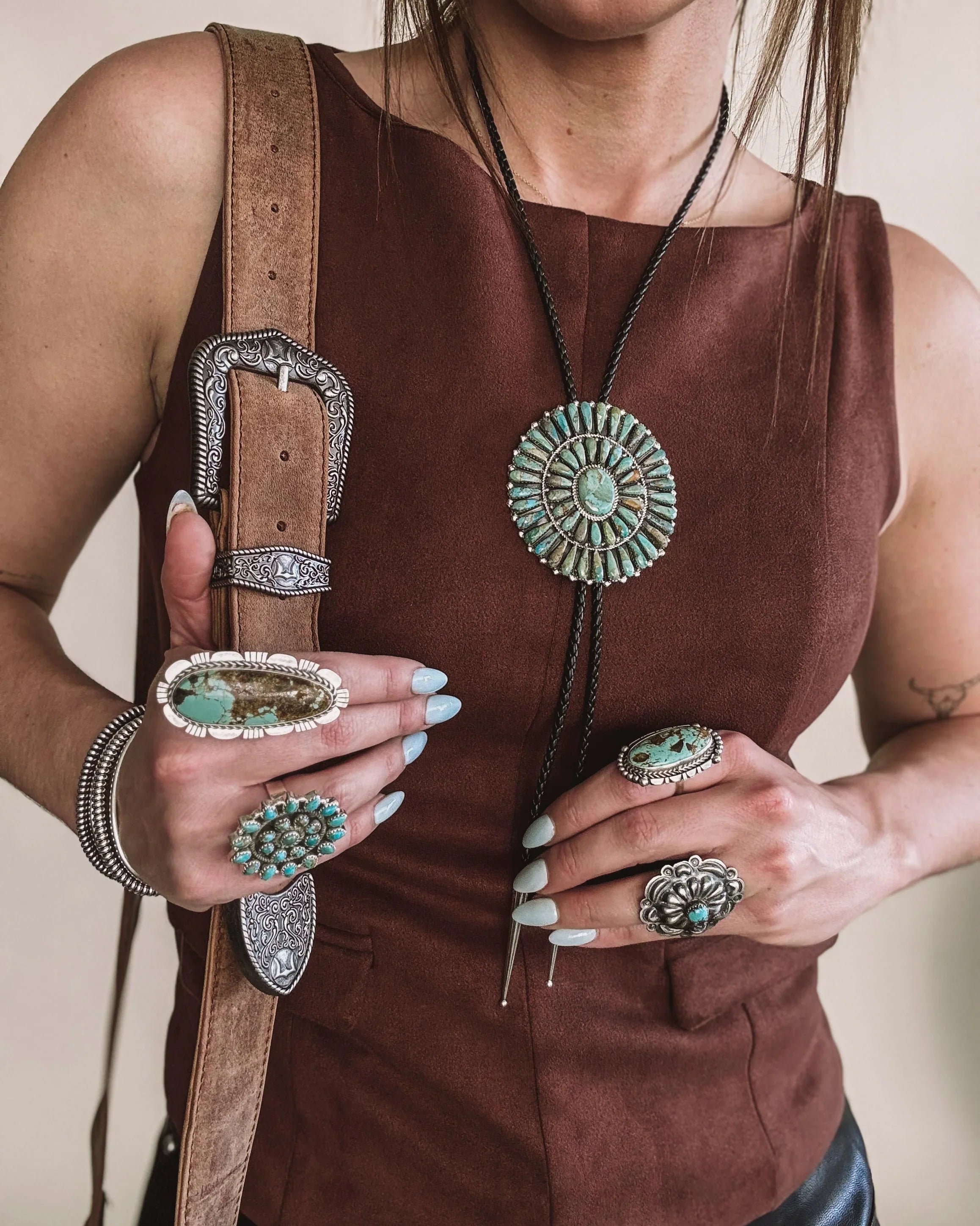 Woman wearing western boho jewelry, turquoise rings, bolo tie necklace, concho belt, brown top