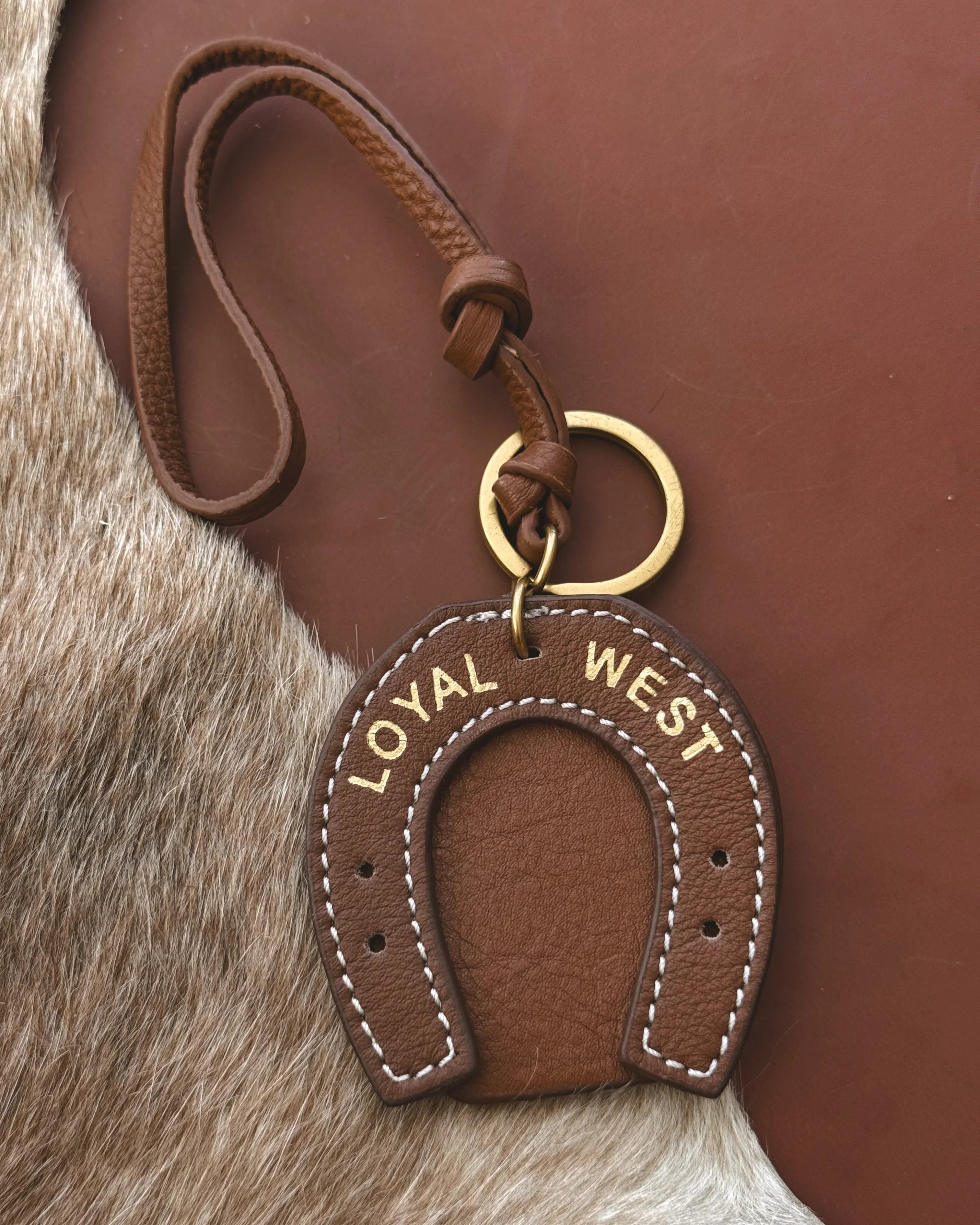 Brown leather keychain with 'LOYAL WEST' text on a fur background