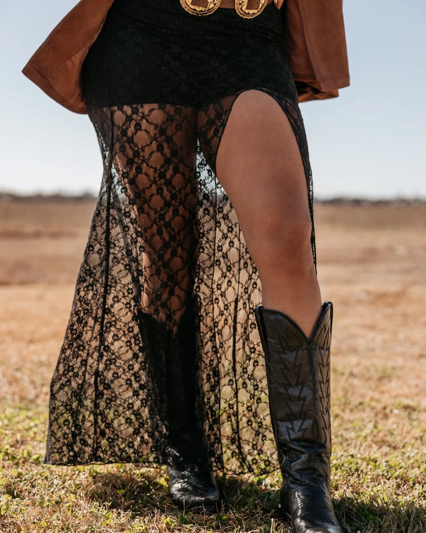 Woman wearing black lace western skirt, concho belt, and cowboy boots in outdoor field
