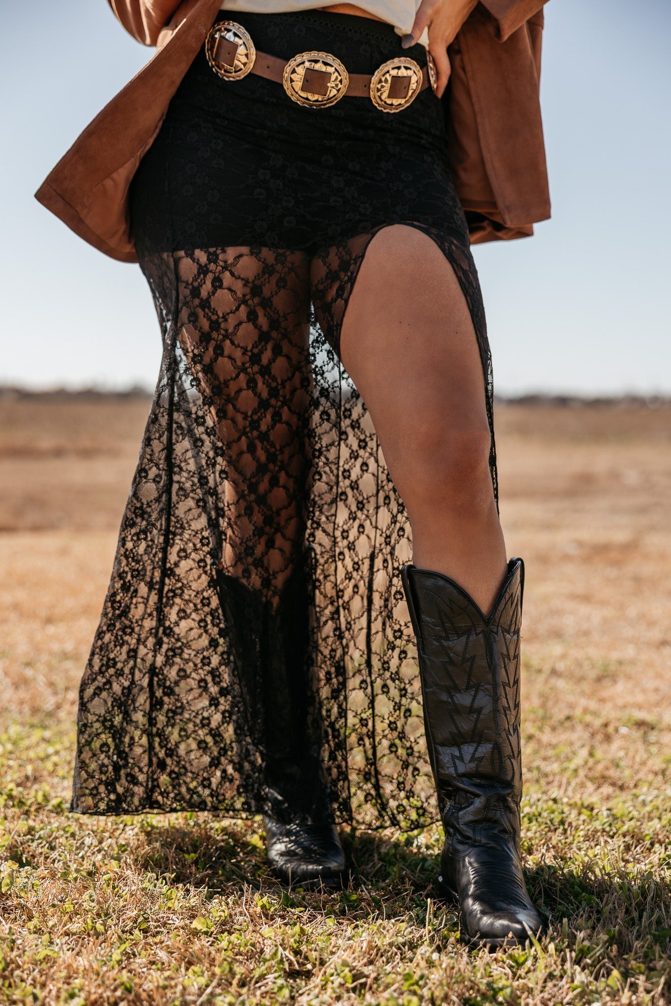 Woman wearing black lace western skirt, concho belt, and cowboy boots in outdoor field
