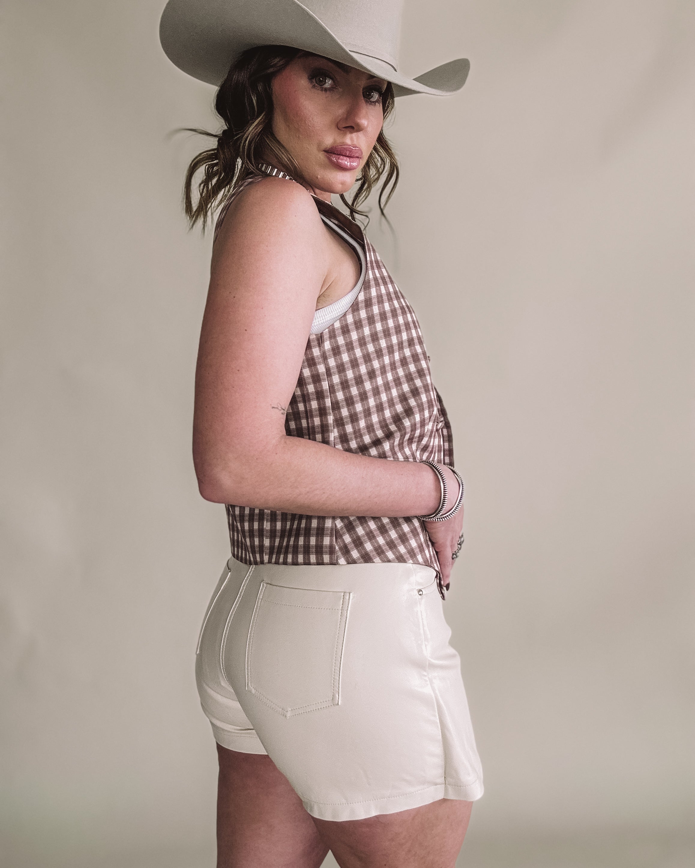 Woman in cowboy hat, gingham halter top, and white shorts, western boho fashion
