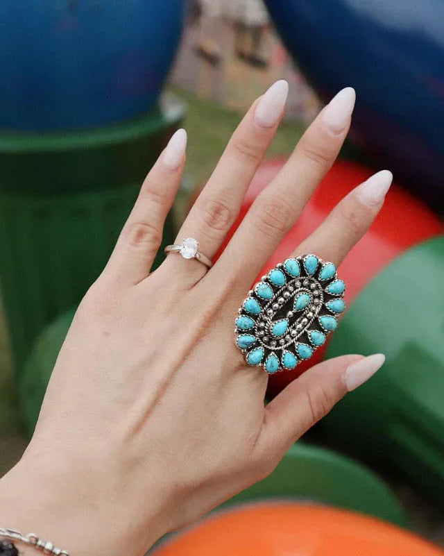 Hand with large turquoise western boho ring and diamond band, colorful background
