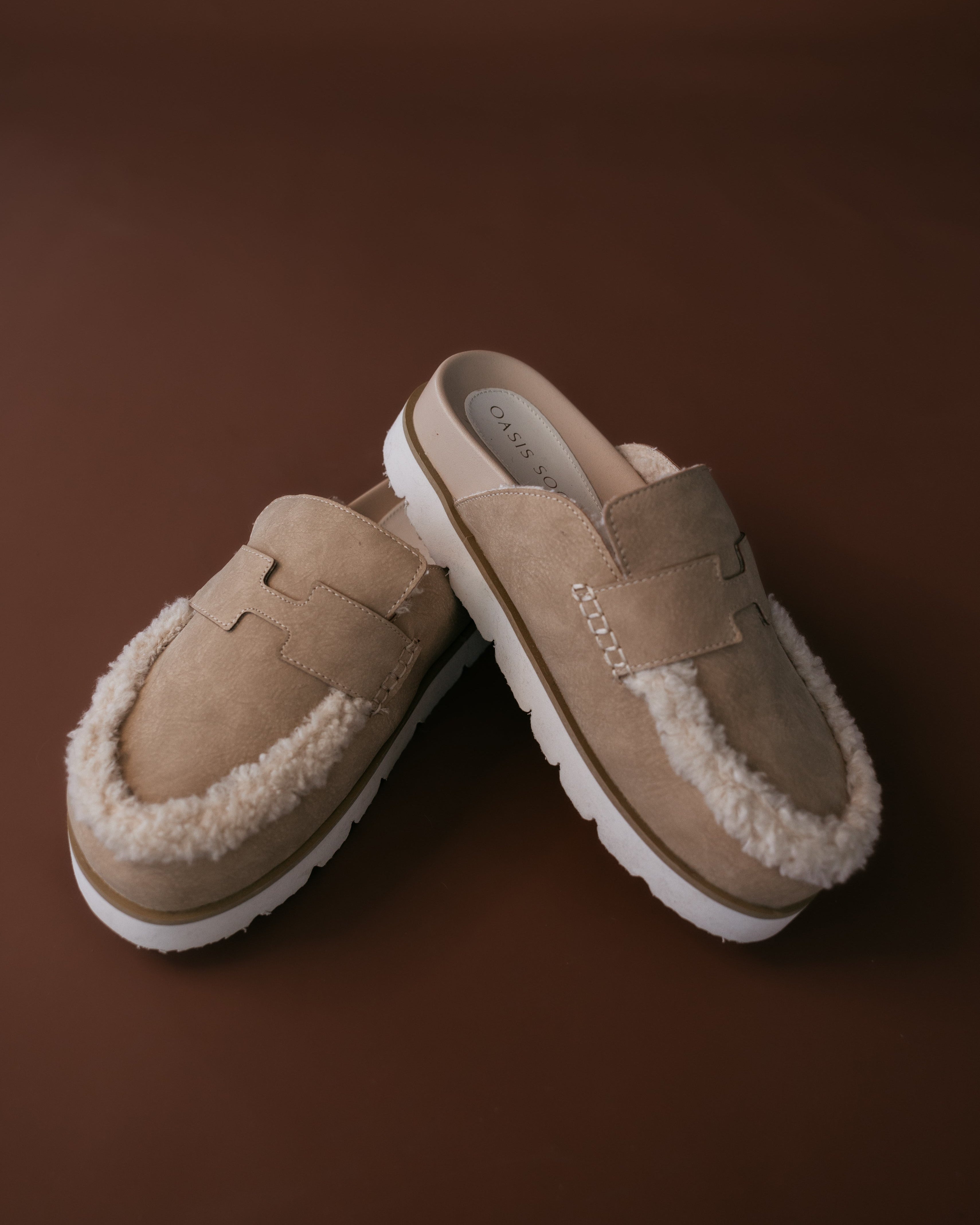 Pair of beige slippers with white fur lining on a brown background
