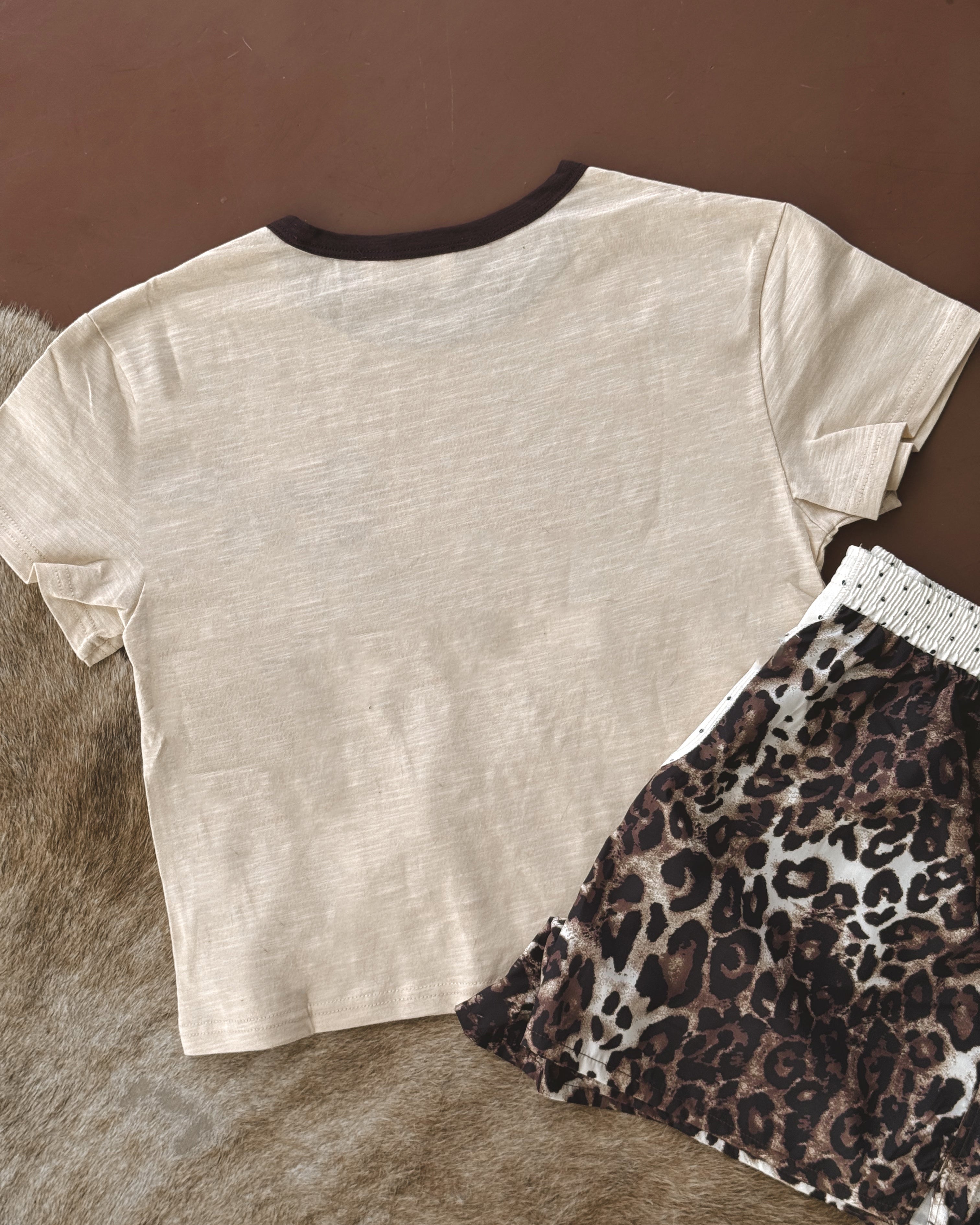 Beige western t-shirt with black collar and leopard print shorts on brown and fur background