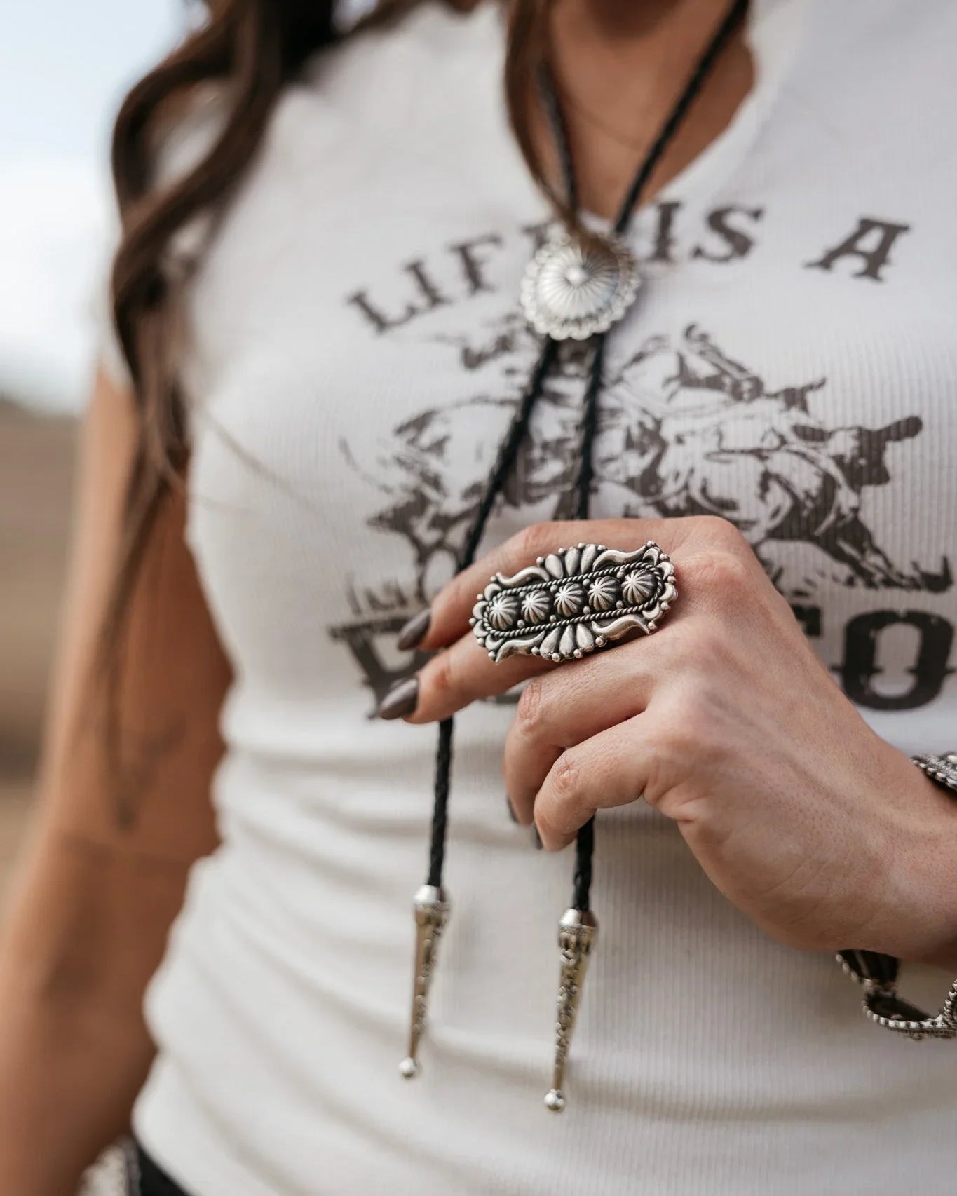Woman wearing western graphic tee, silver statement ring, and concho bolo tie