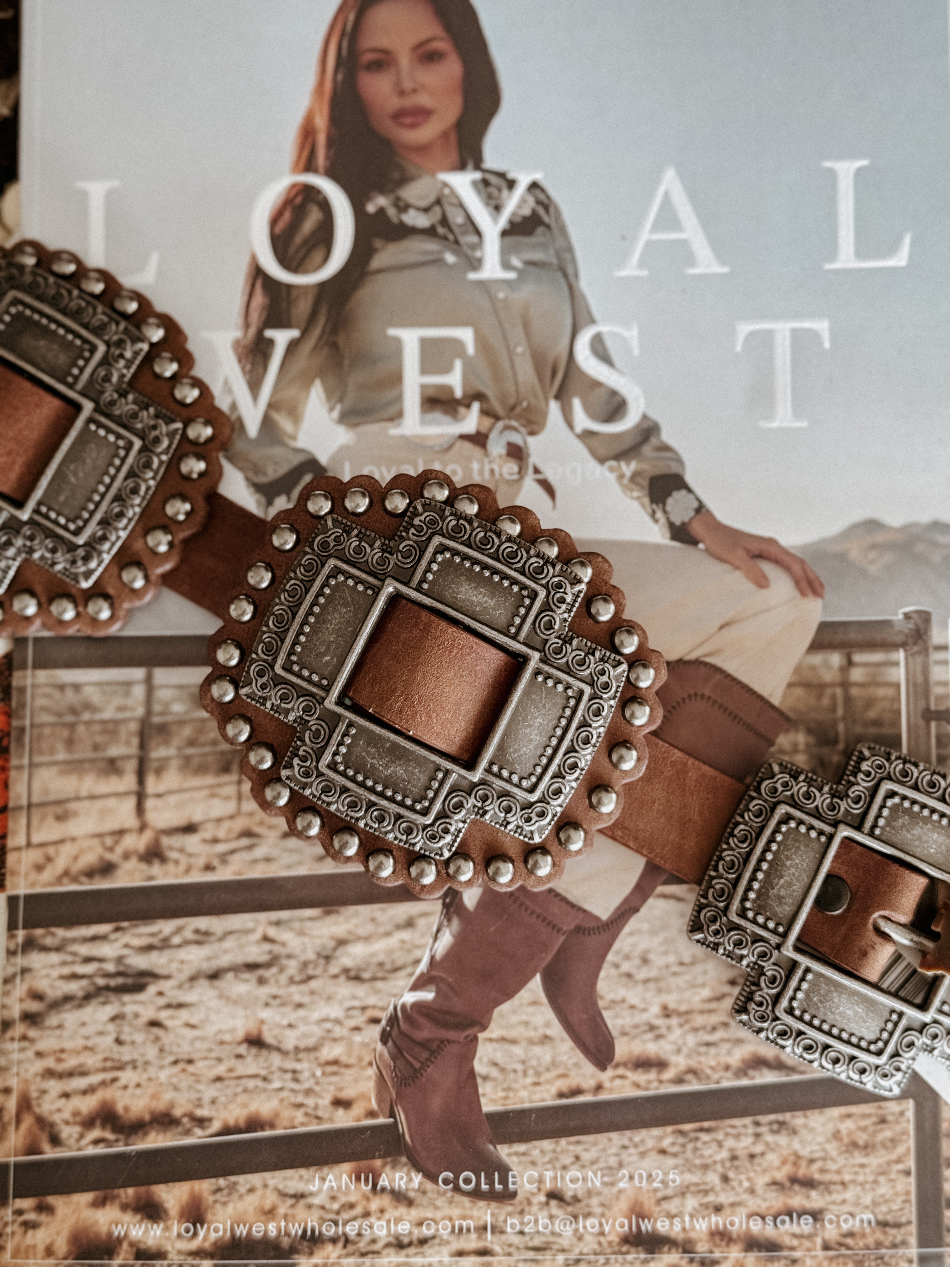 Western boho concho belt with ornate silver buckles resting on a magazine featuring a woman in cowgirl boots and western outfit outdoors.