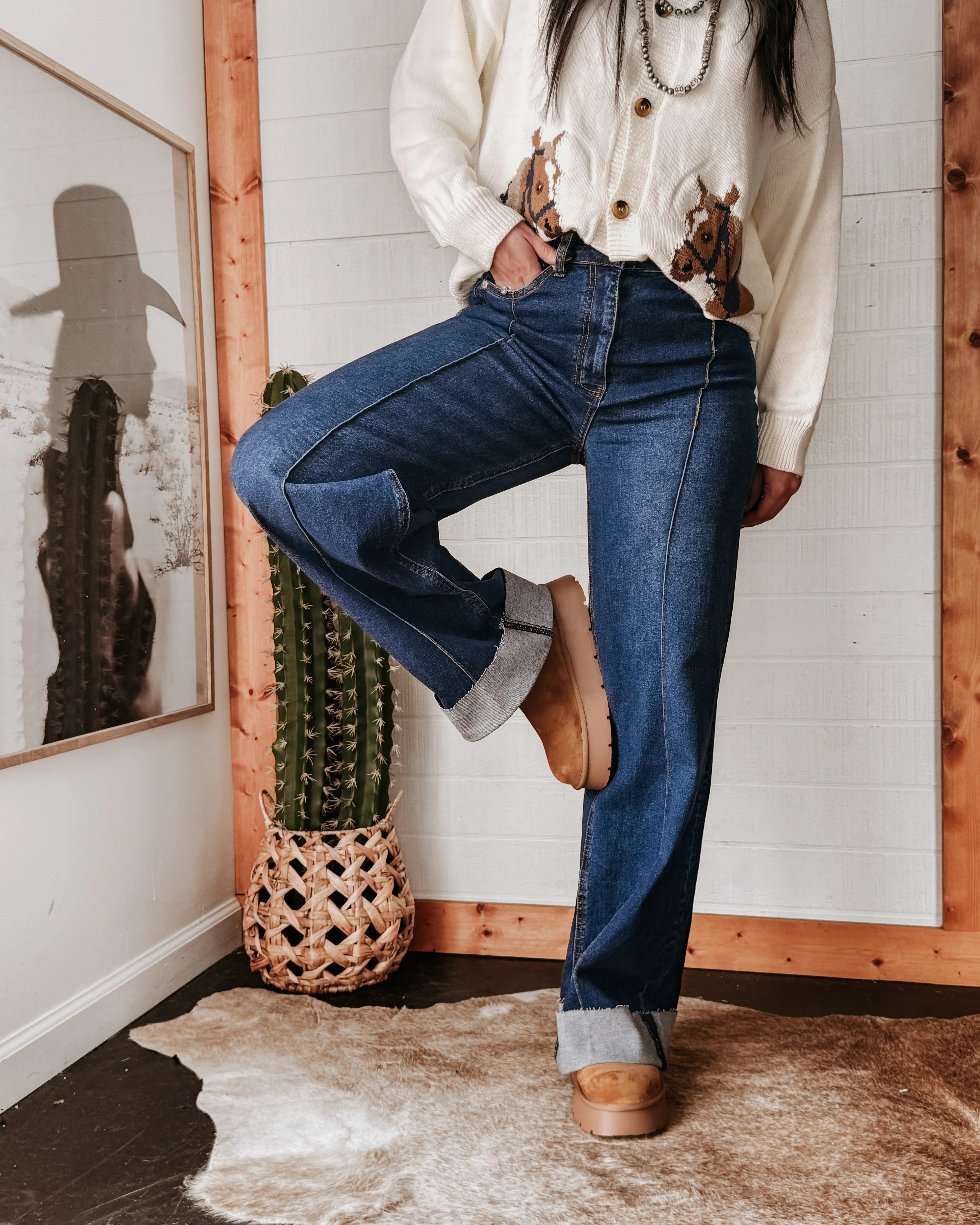 Woman modeling high rise hem jeans with rolled cuffs, western boots and cowgirl sweater