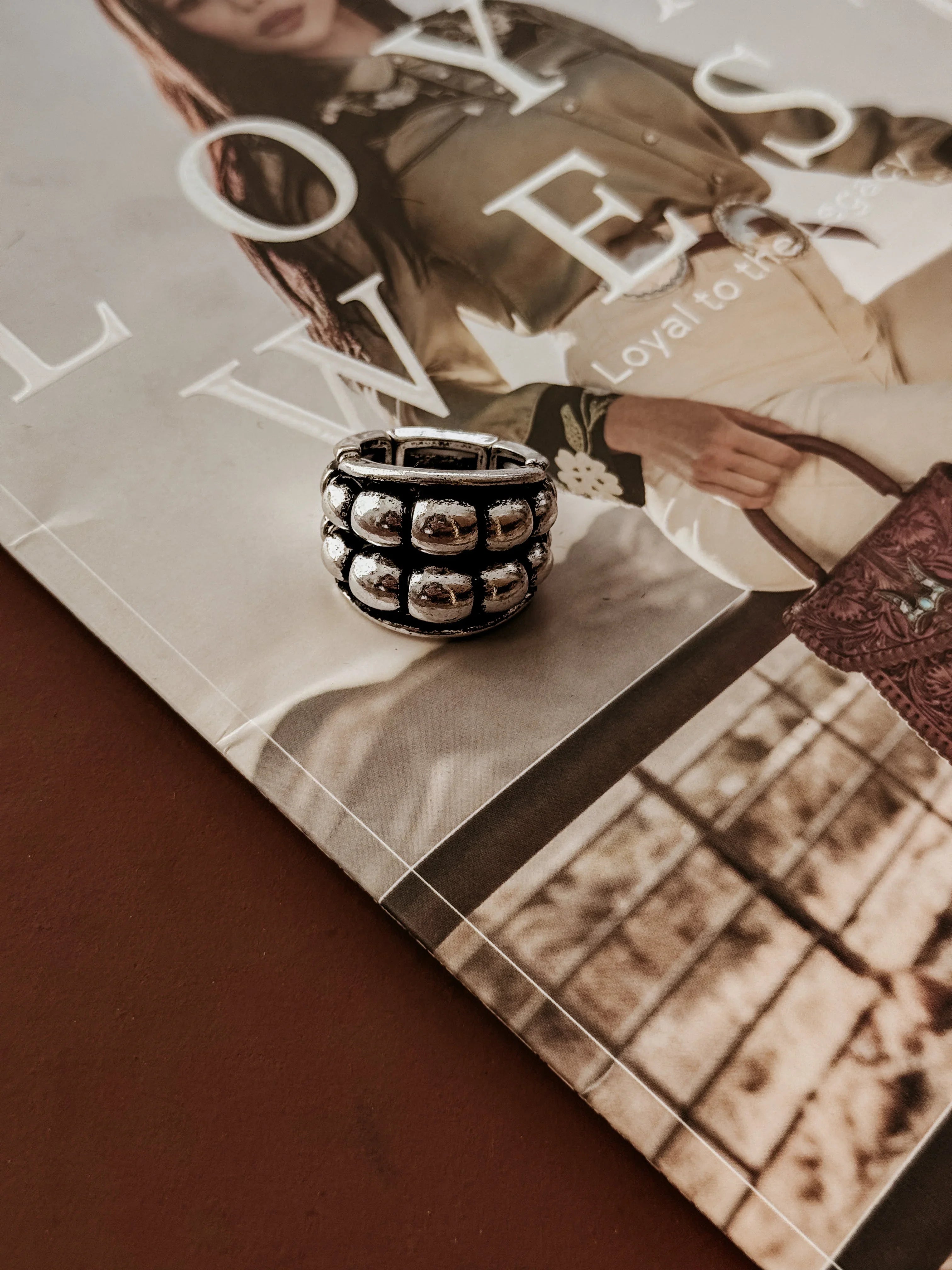 Silver ring with textured bubble design on a magazine with blurred text and images