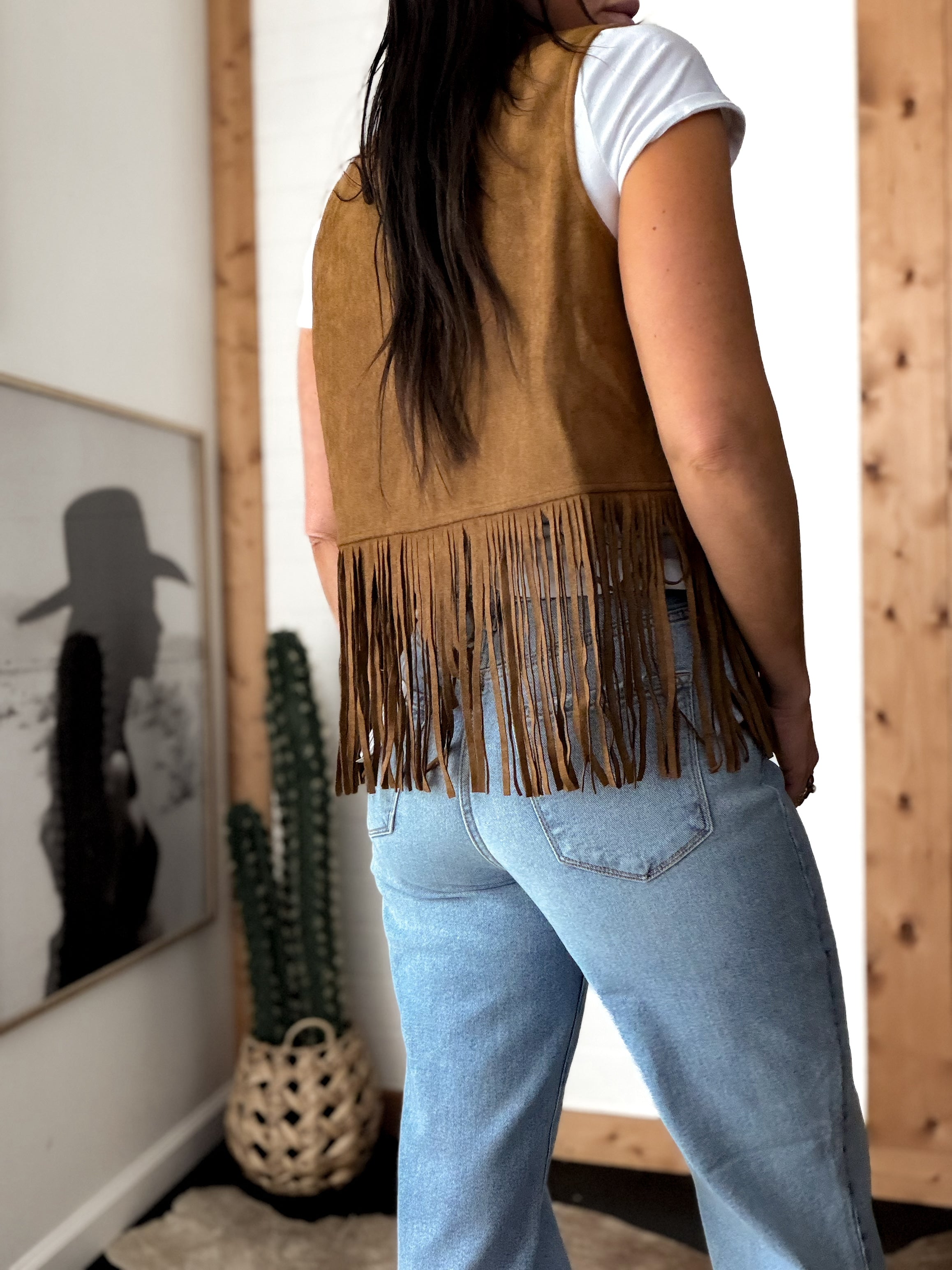 Woman in light wash jeans and brown suede fringe vest, western boho style indoors