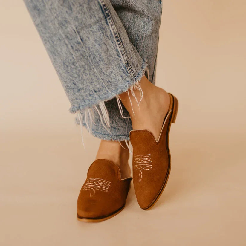 Brown loafers worn with light blue jeans on a beige background