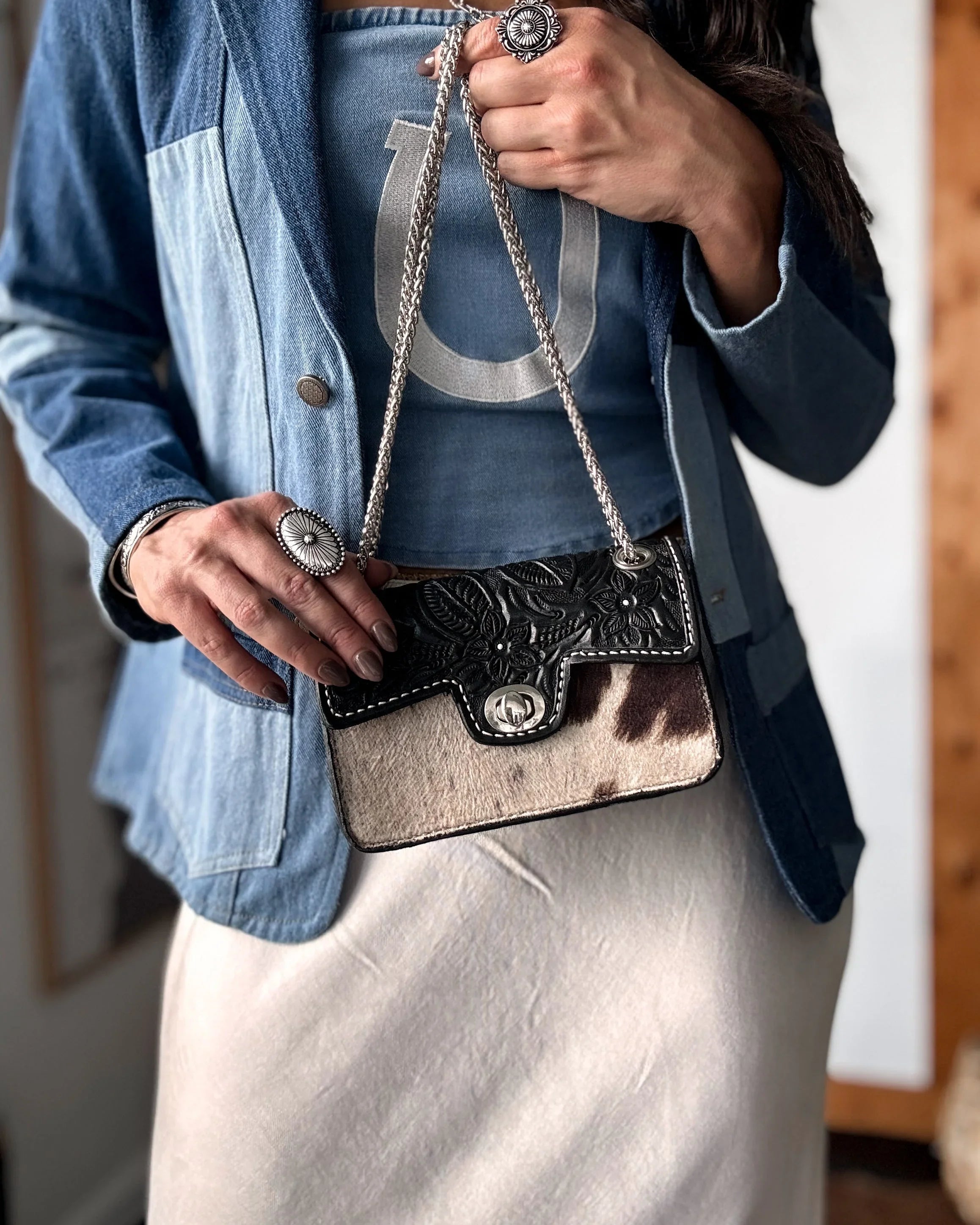 Person holding a decorative cowhide handbag with a blue jacket and white pants.