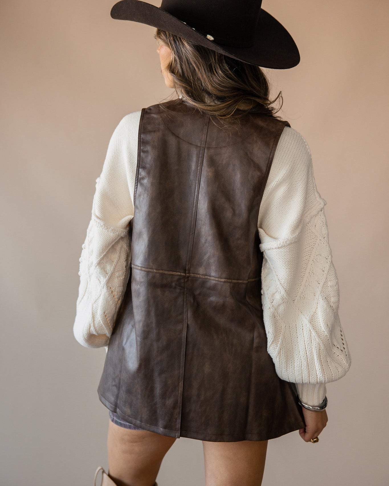 Woman in brown faux leather dress, cream knit sleeves, cowboy hat and boots, western style