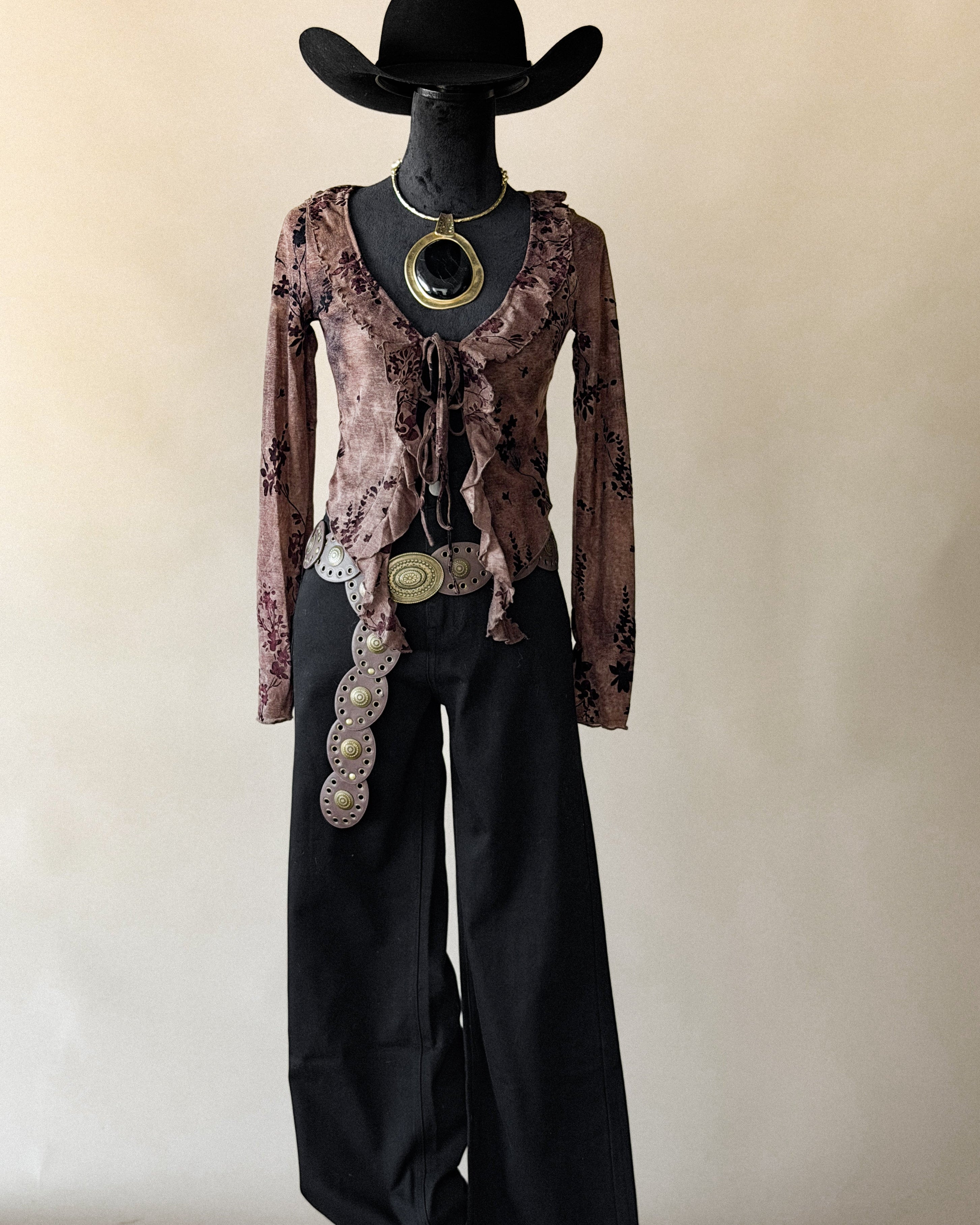 Mannequin wearing a floral top, black pants, and a cowboy hat with a beige background