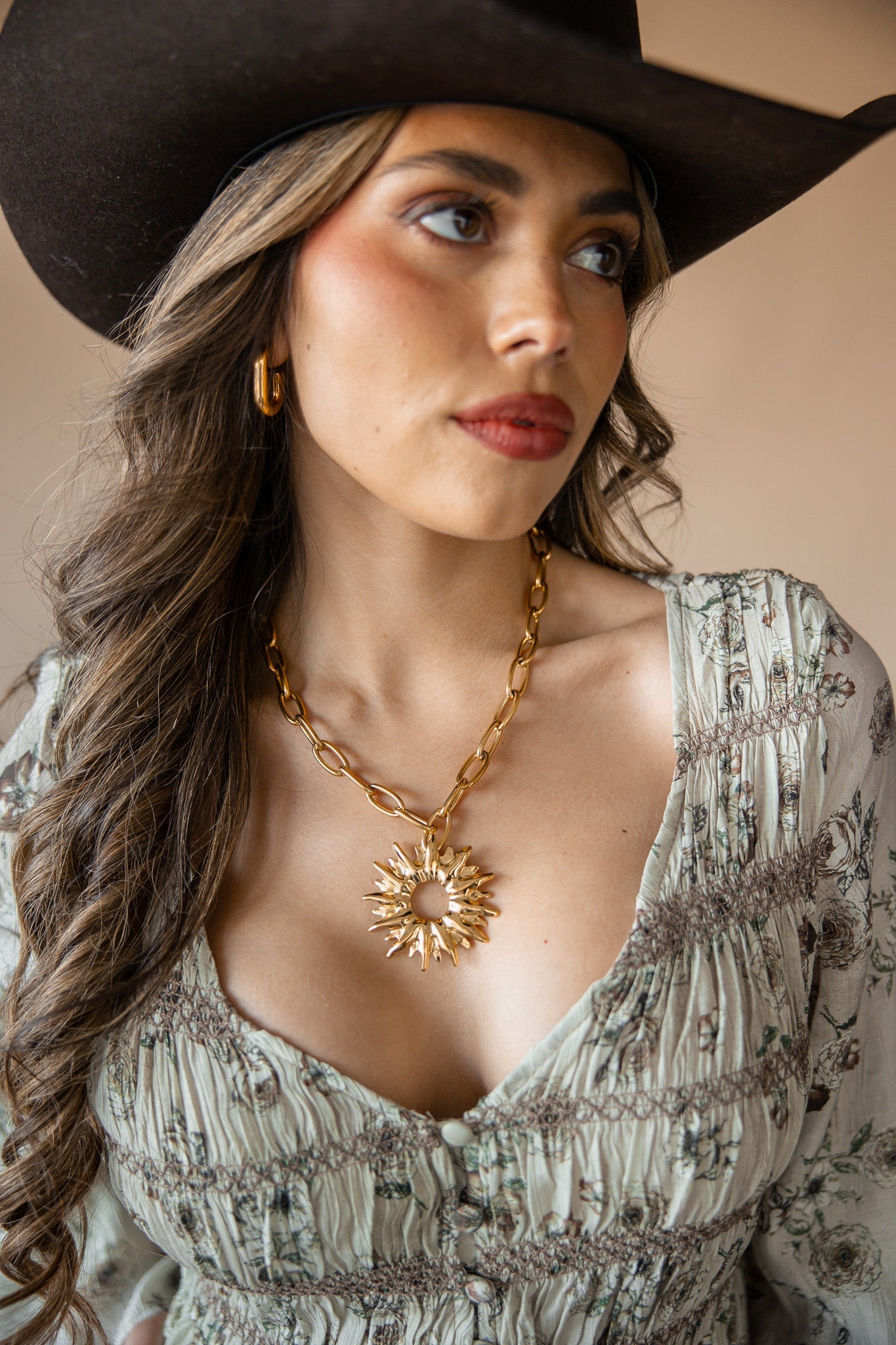 Woman wearing a cowboy hat, floral dress, and gold necklace with a star pendant.