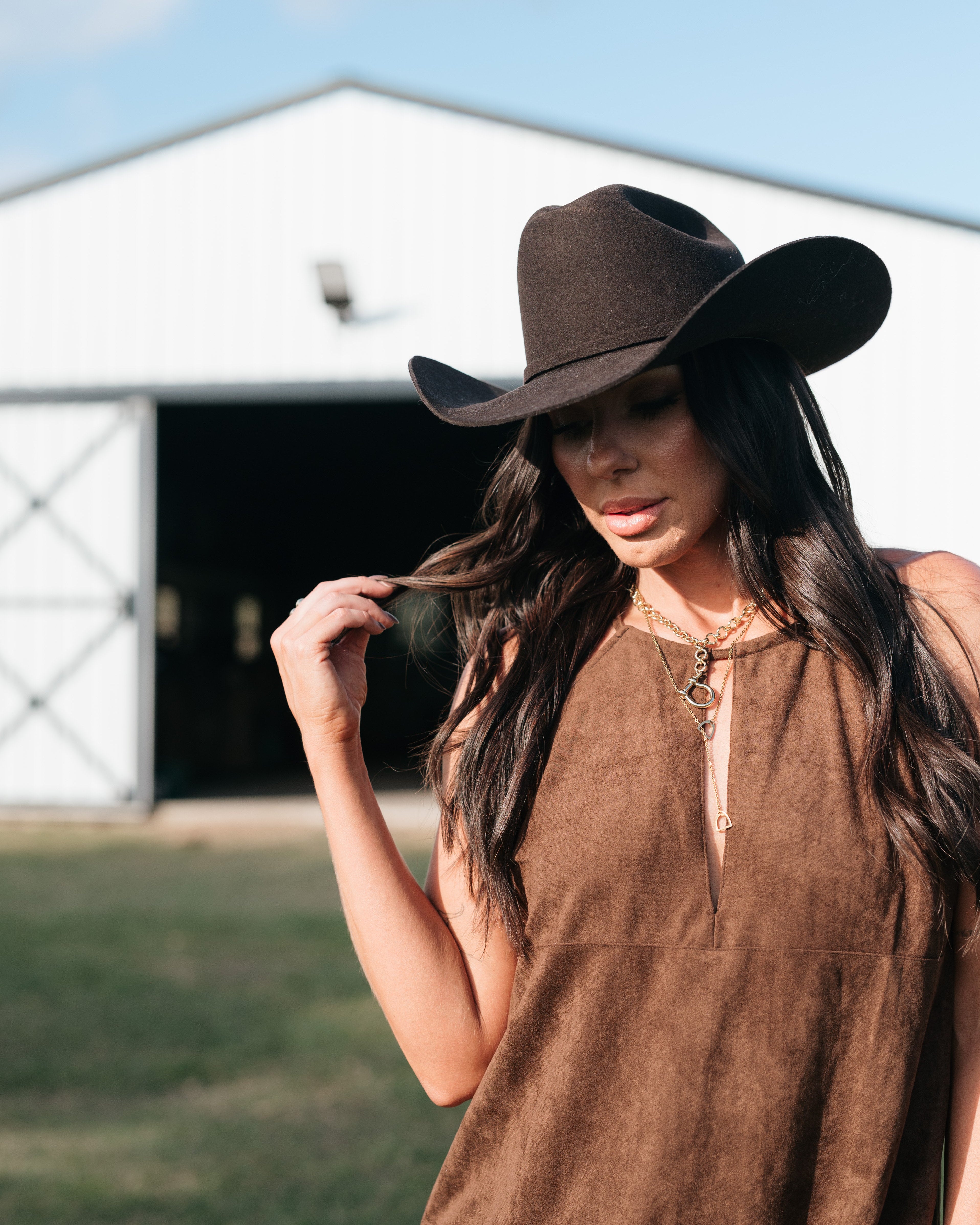 Woman in brown suede western dress and black cowboy hat outside barn, western boho style