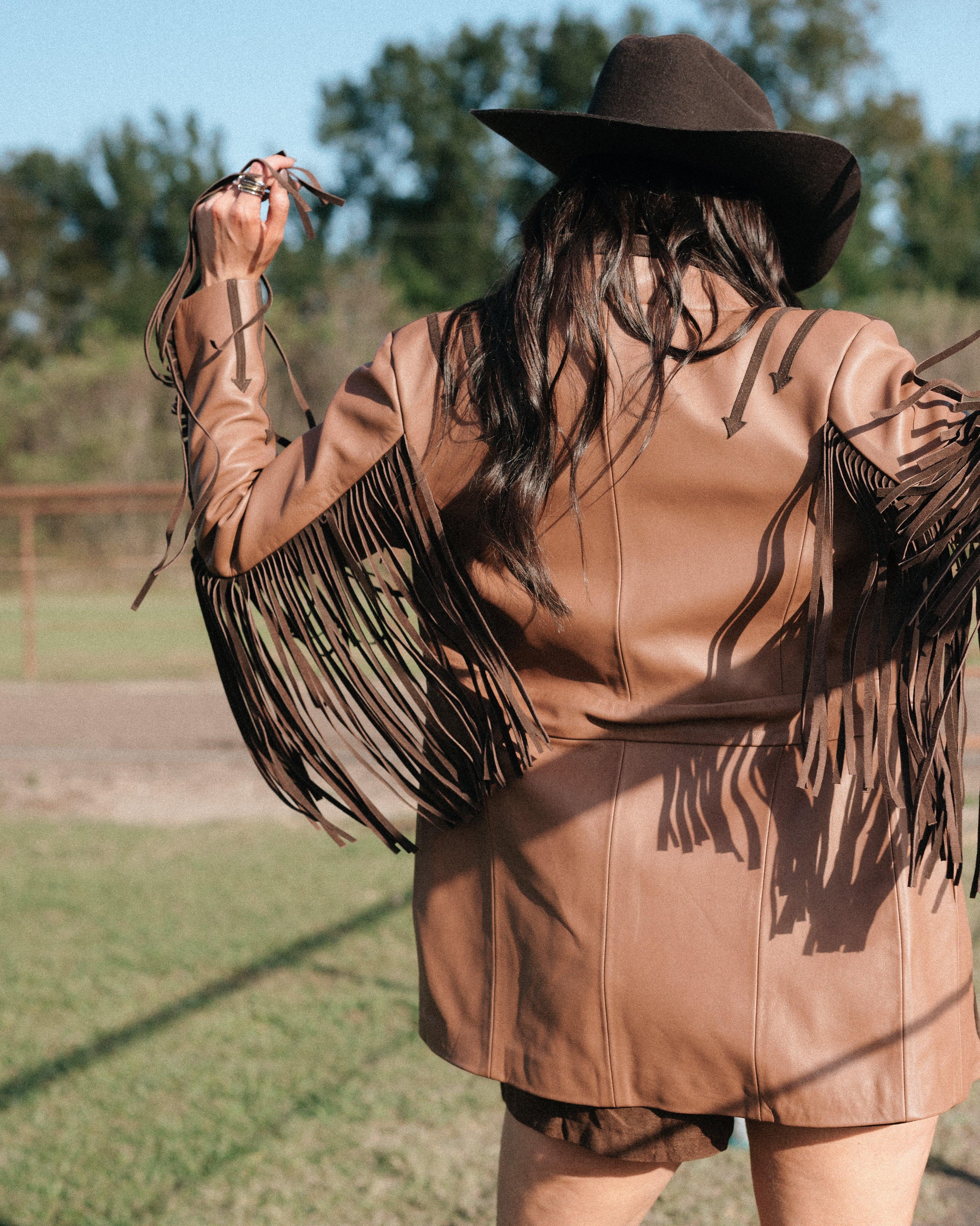 Woman in brown fringe western jacket and cowboy hat outdoors