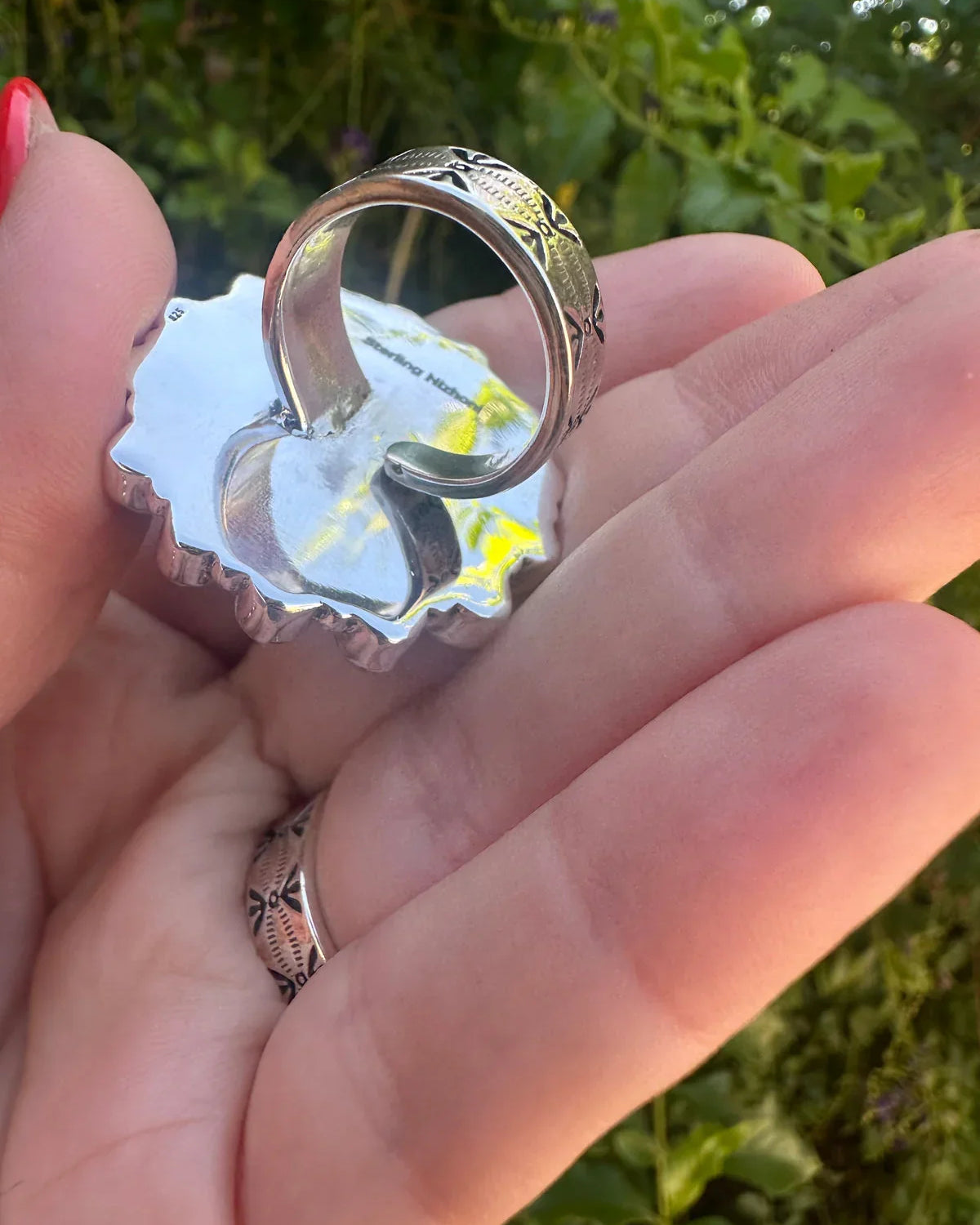 Hand holding a sterling silver horse ring with western engraved details outdoors