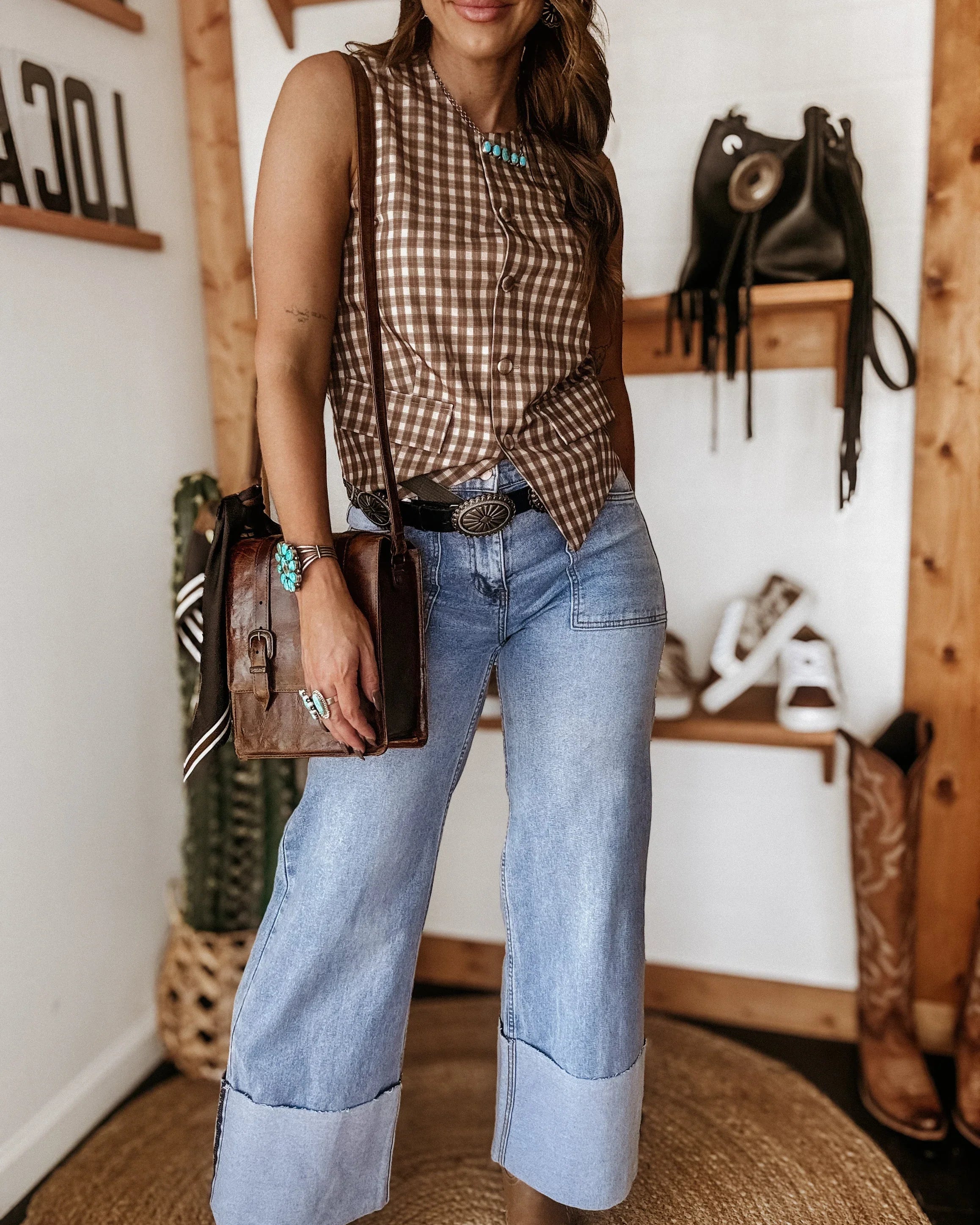 Woman in western wide leg jeans, sleeveless plaid top, turquoise jewelry, and cowgirl accessories
