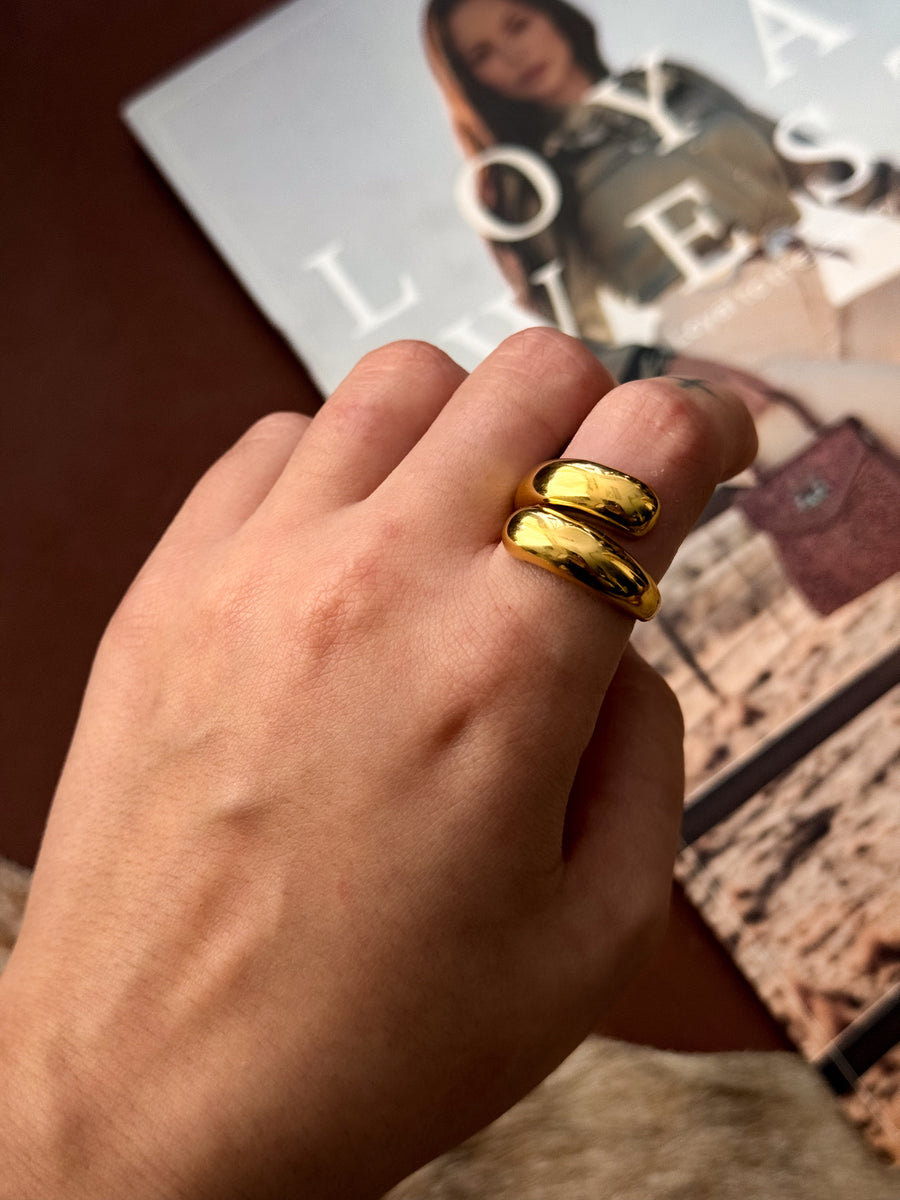 Close-up of a hand wearing a chunky gold statement ring with a double-band design, resting over a fashion magazine.