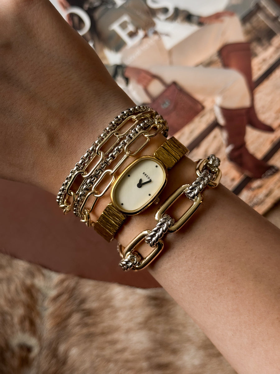Gold watch and bracelets on a wrist with a magazine in the background